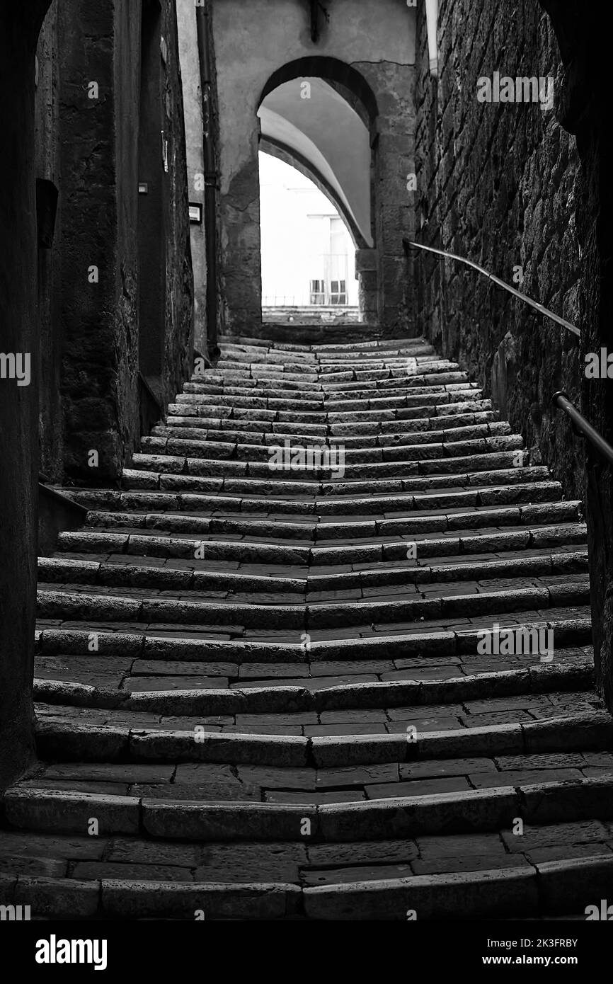 Una ripida strada lastricata con le scale e un cancello in pietra nella città di massa Maritima in Italia, monocromatica Foto Stock