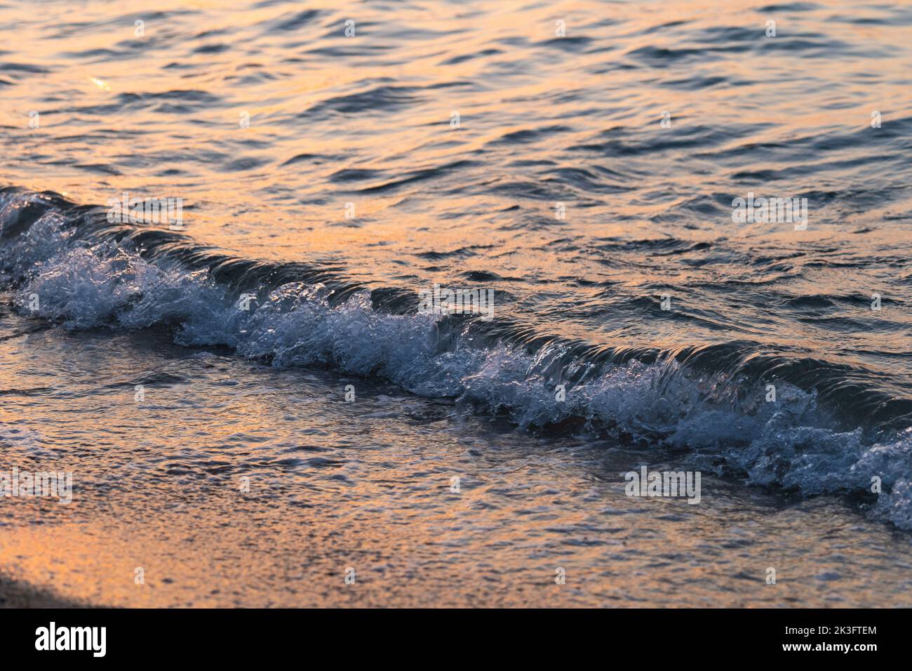 L'onda di mare spruzza da vicino. Ondulazione della superficie dell'acqua di mare con luce dorata del tramonto. Foto Stock