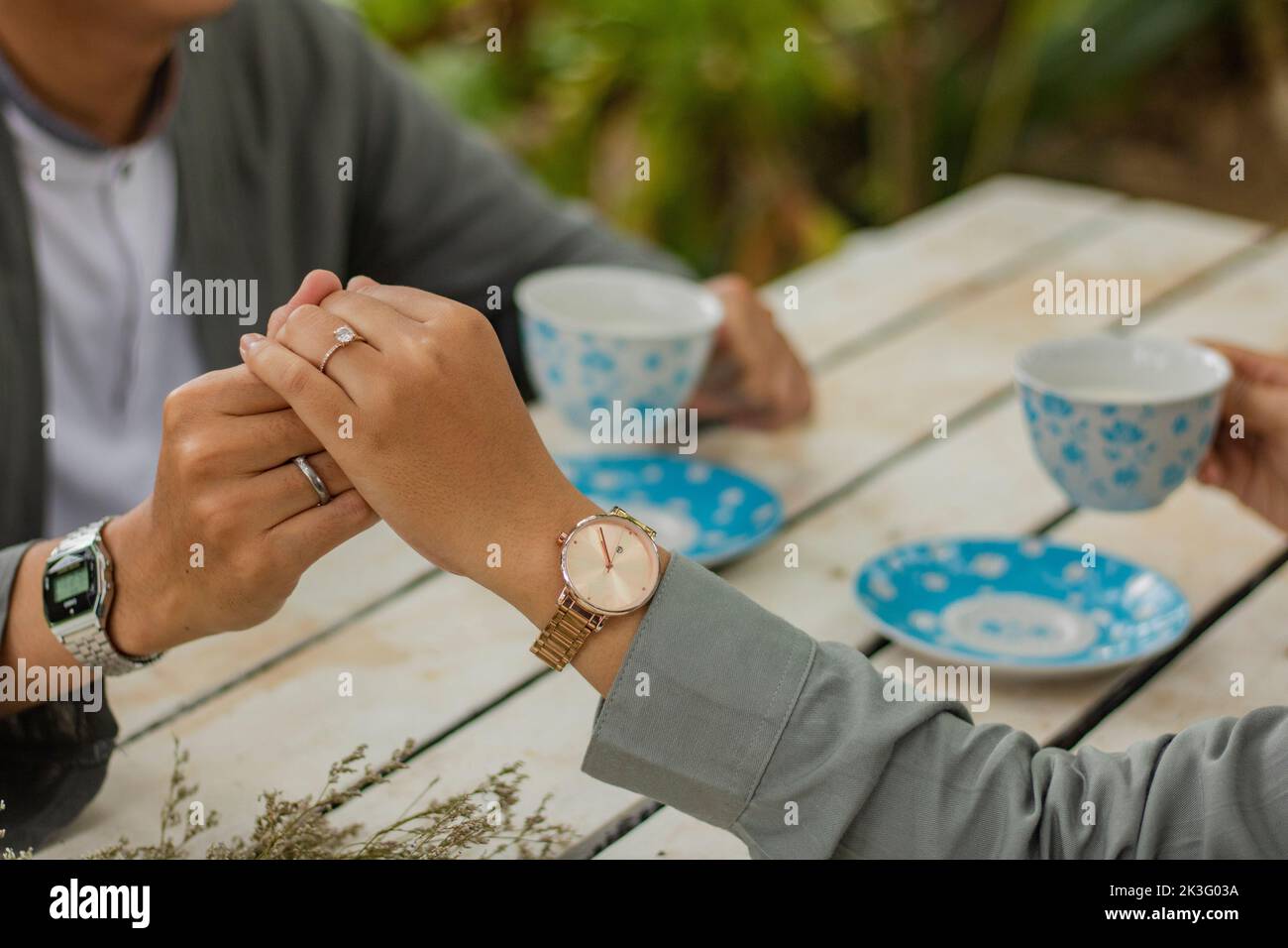 primo piano di una giovane coppia felice che tiene le mani l'una con l'altra e che si gode una tazza di bevanda nel caffè Foto Stock