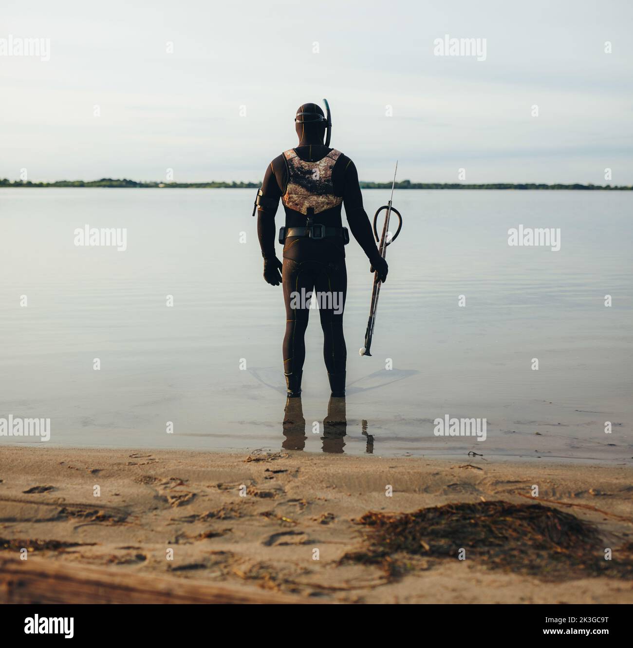 Vista posteriore del pescatore della lancia in piedi nell'acqua con un fucile a lancia. Giovane uomo avventuroso che si prepara ad andare a pesca di spearfishing in mare. Foto Stock