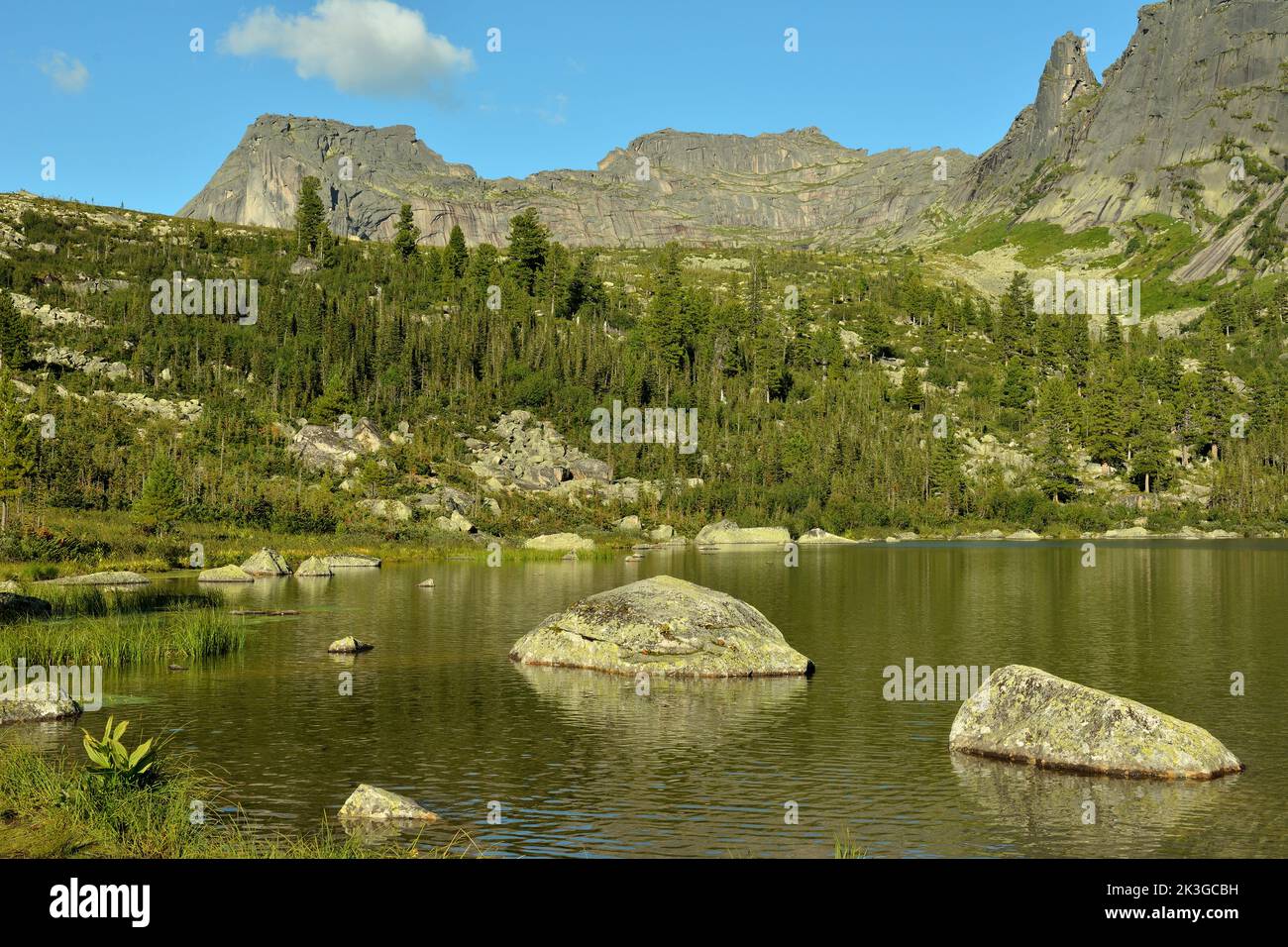 Massi di pietra in un pittoresco lago in una pineta sullo sfondo di una montagna di forma insolita. Rainbow Lake e Monte Sayan addormentati, Erga Foto Stock