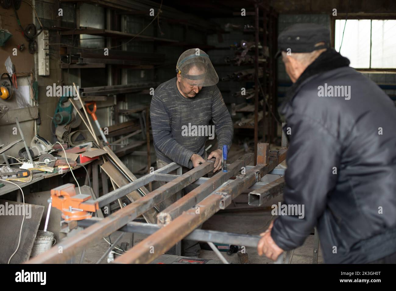 La saldatrice trattiene il metallo. Persone in officina metallo. Lavori in garage. Operatore nella maschera protettiva. Foto Stock