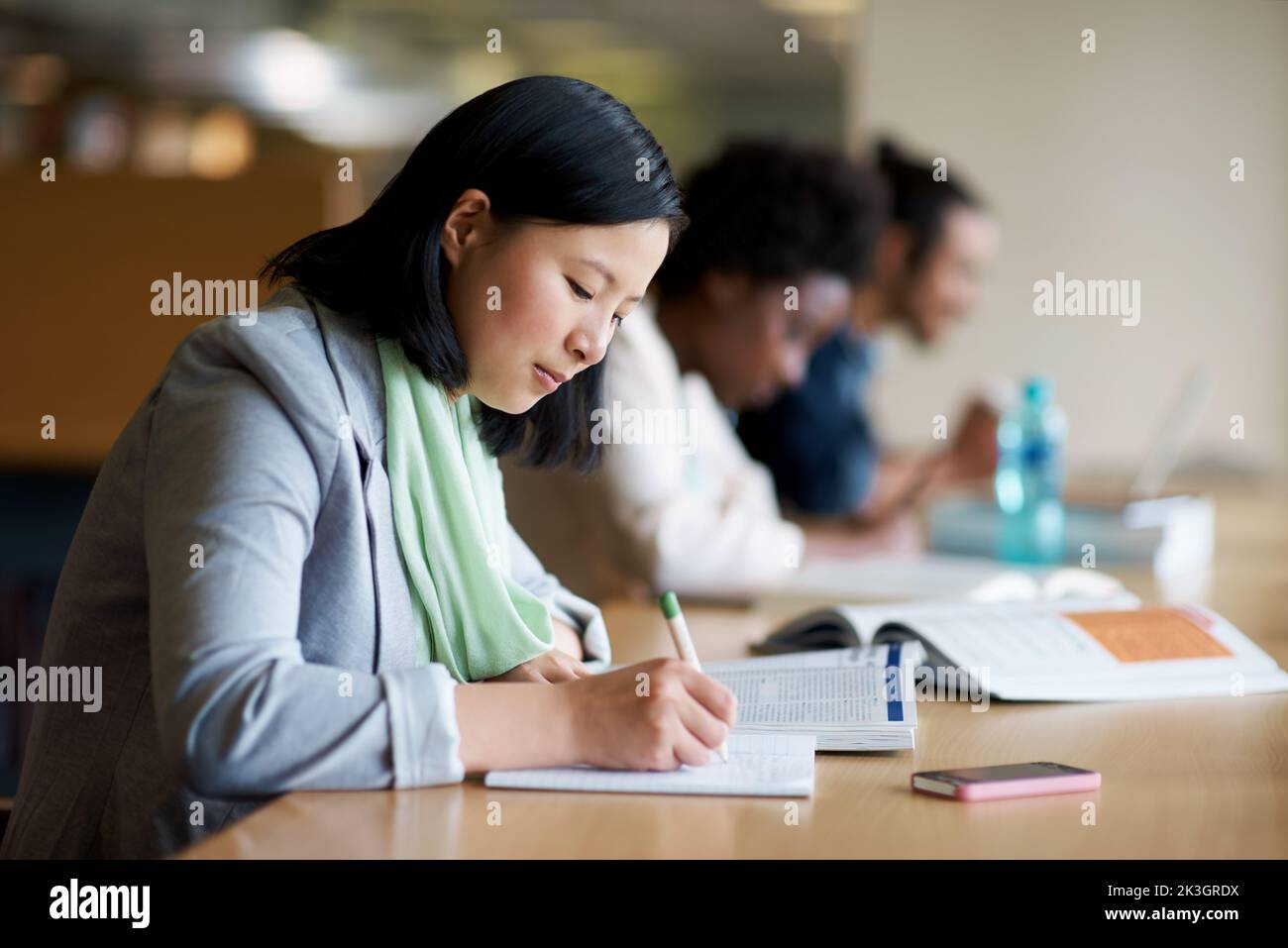 Cramming alcune conoscenze dell'ultimo minuto. Una giovane donna che studia in biblioteca con altri studenti. Foto Stock