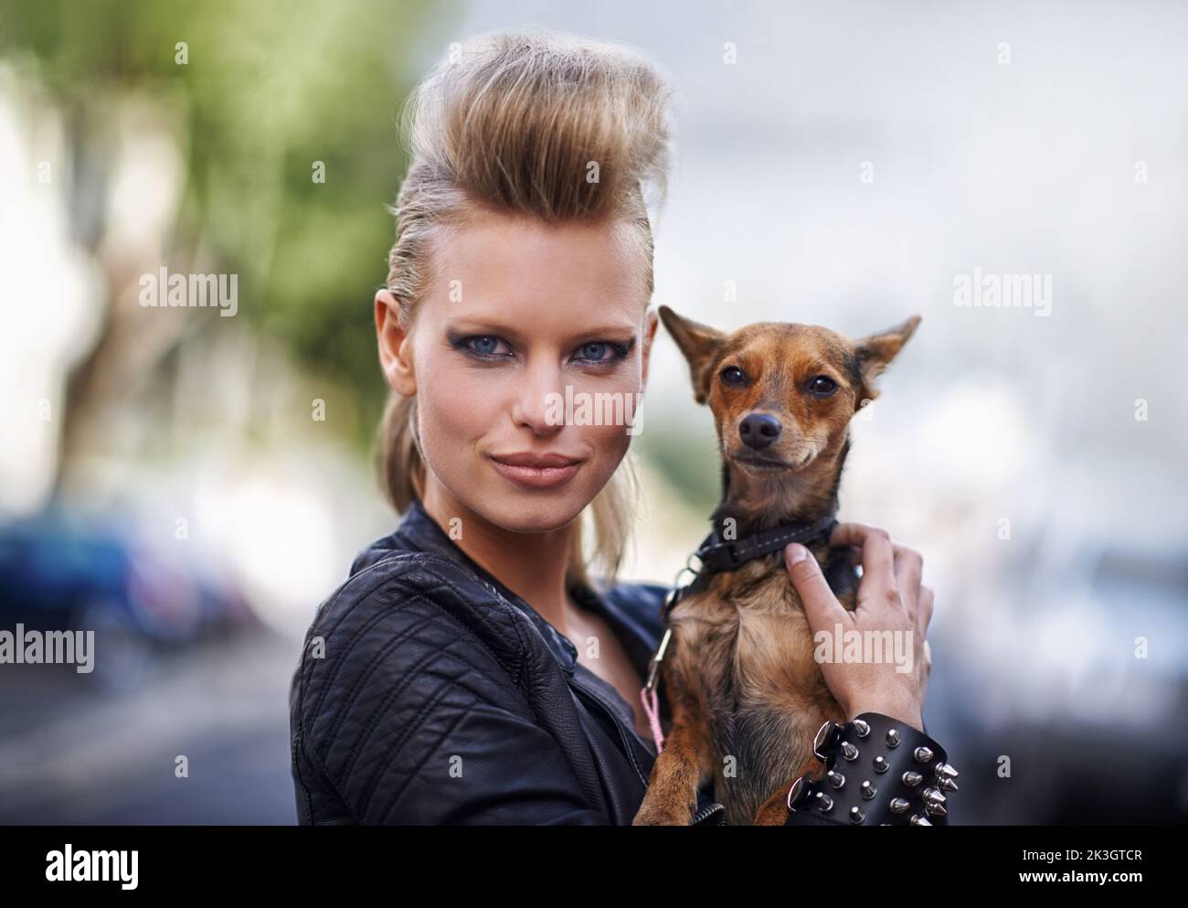 HES l'animale domestico perfetto per una rockstar. Una bella giovane donna alla moda che tiene il suo piccolo cane in una strada cittadina. Foto Stock