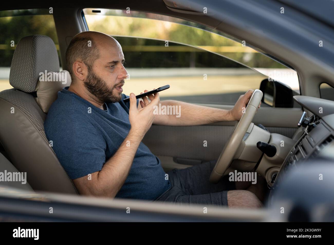 uomo alla guida della sua nuova auto che registra il messaggio vocale sullo smartphone, conducente che utilizza il registratore di comandi vocali sul telefono Foto Stock