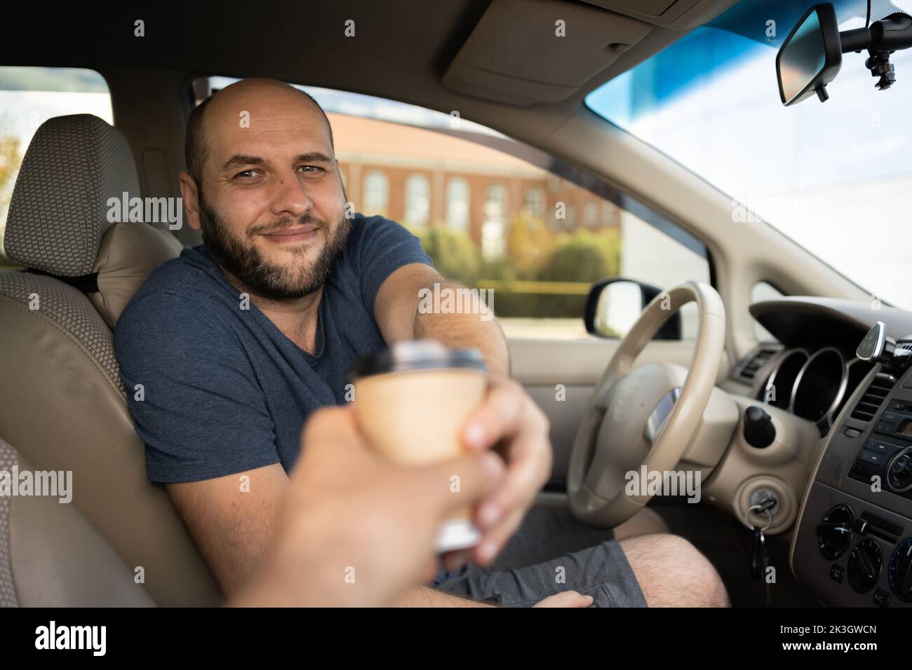 ritratto di un uomo seduto in auto e l'acquisto di caffè per andare. l'uomo alla guida della sua auto e tenendo il caffè, mentre evincendo gioia Foto Stock