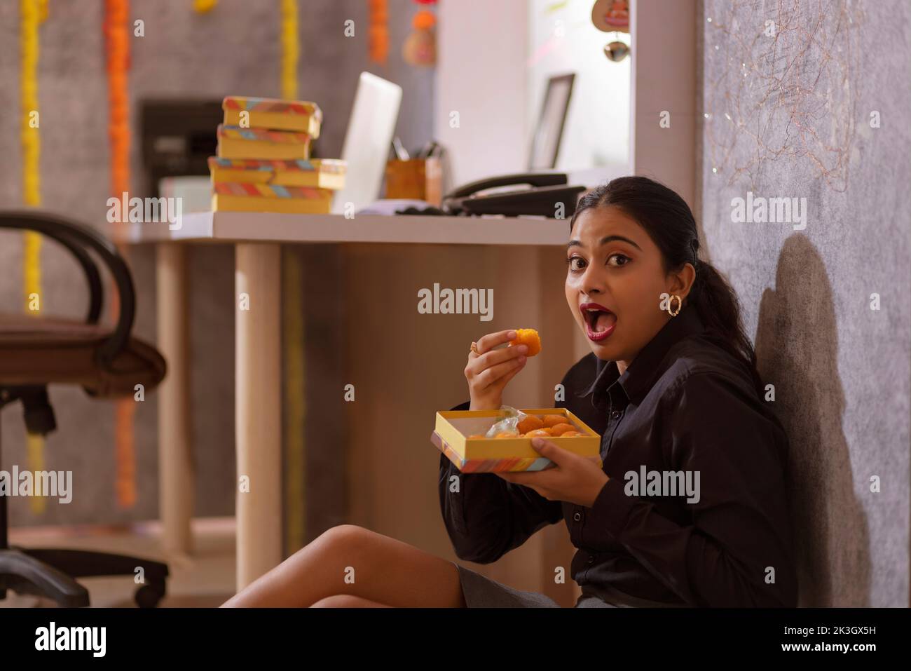 Donna dipendente che mangia dolce in ufficio durante la celebrazione Diwali Foto Stock