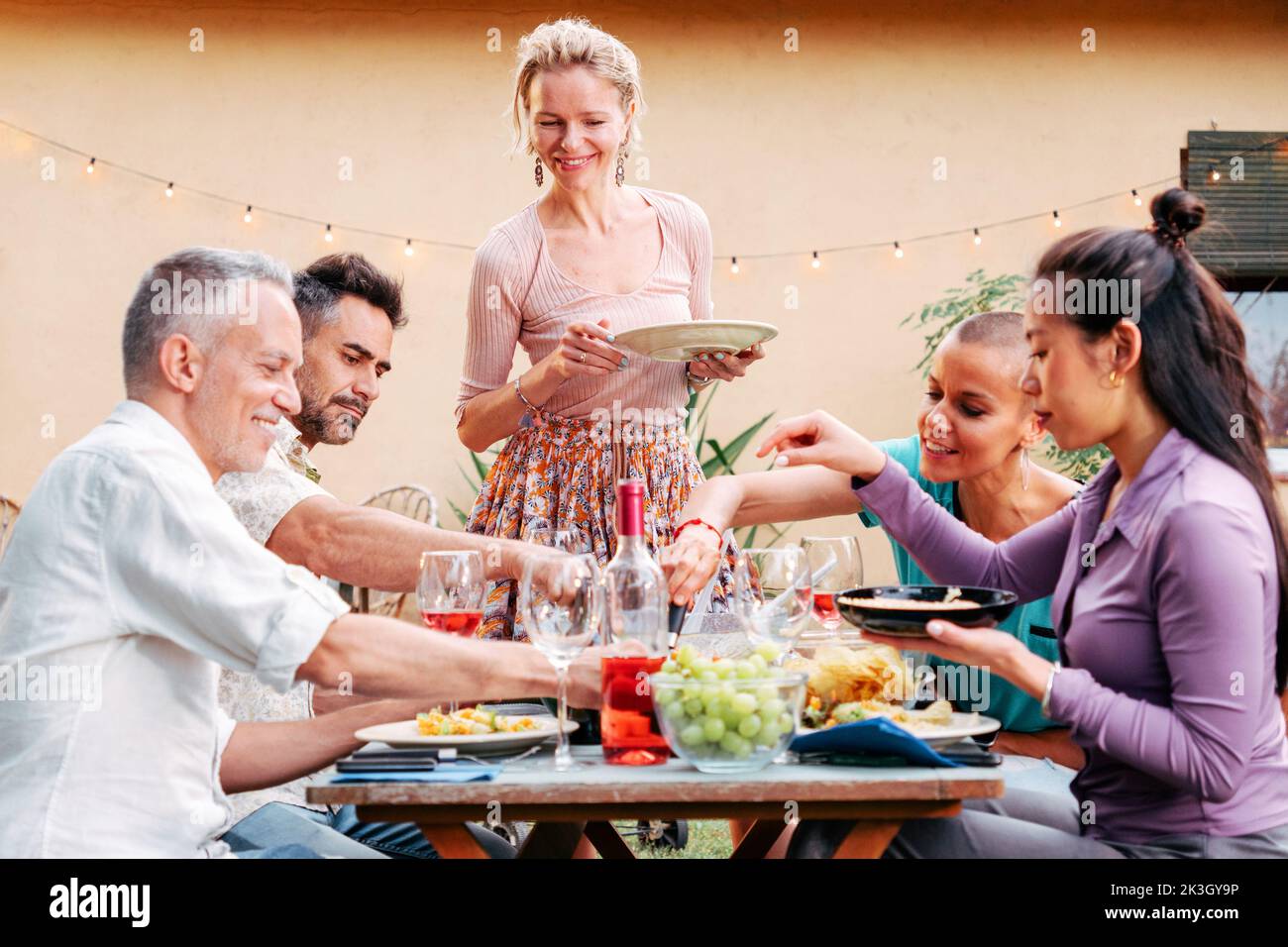 Donna matura che serve cibo agli amici e divertirsi in una riunione barbecue. Gruppo di amici adulti che hanno una cena all'aperto nel cortile posteriore Foto Stock