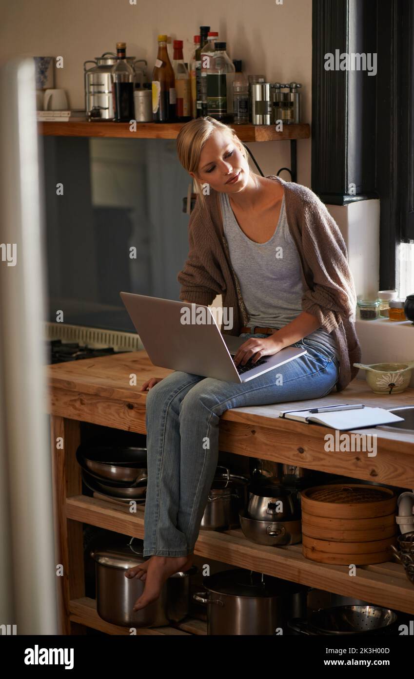 Il blogging alimentare è una passione. Una donna attraente seduta sul suo bancone della cucina usando un laptop. Foto Stock