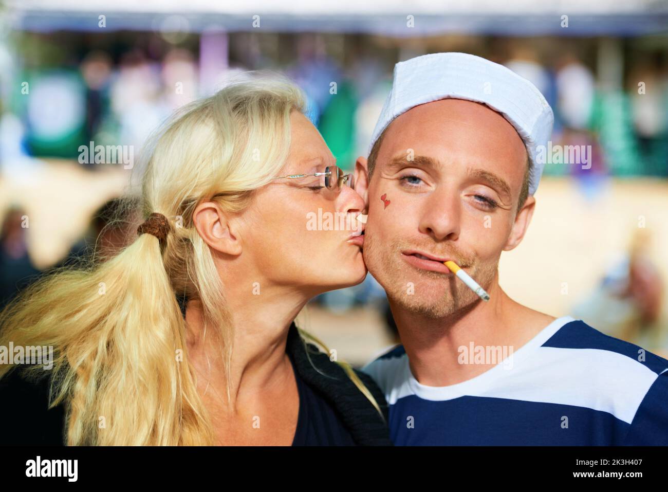 Nessuno poteva resistere al marinaio. Una donna bacia un ragazzo in un vestito di marinaio in un festival di musica. Foto Stock