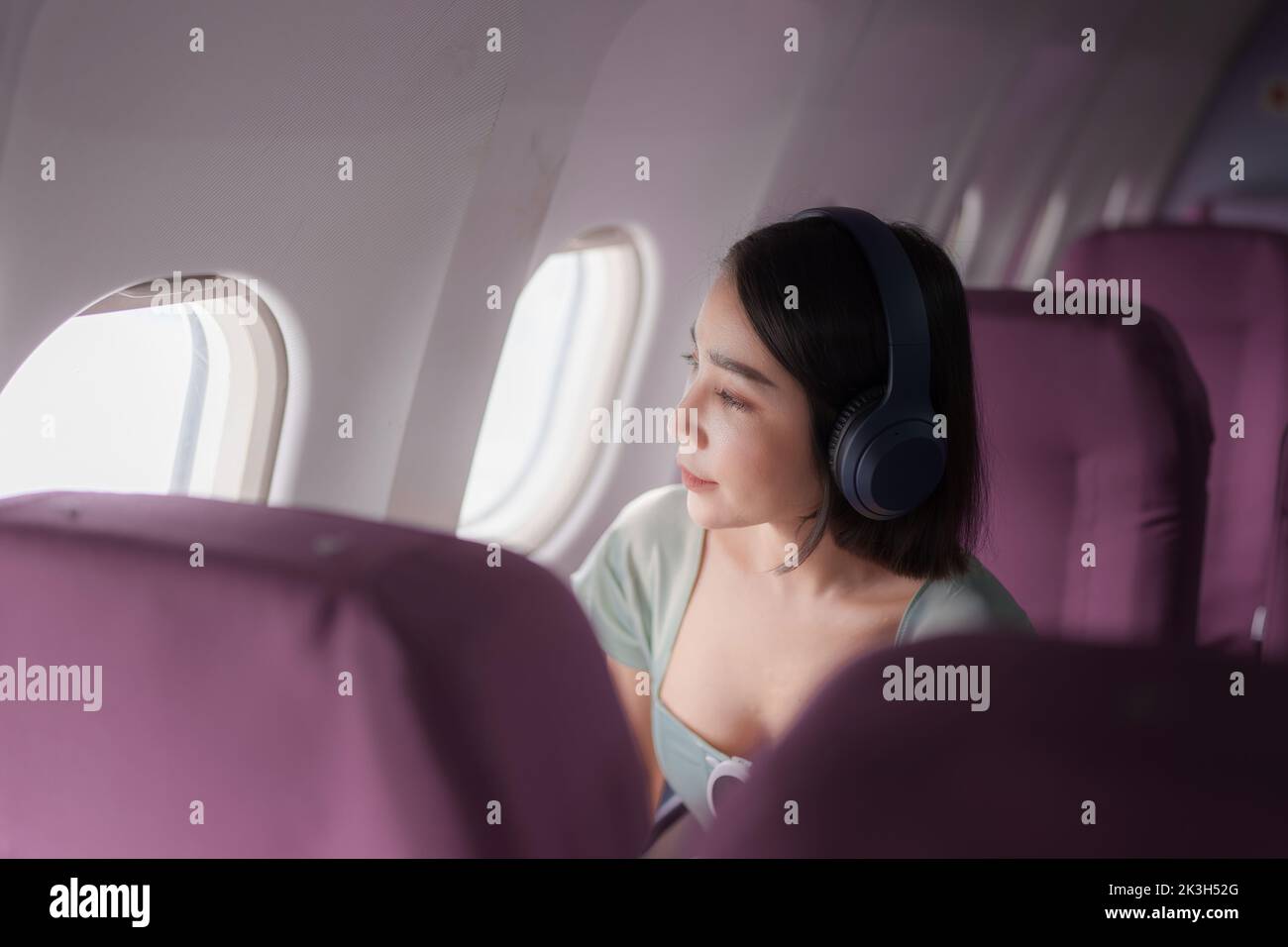 Giovane donna asiatica indossa cuffie per la ricerca di canzoni con cancellazione del rumore nel negozio online sull'app durante il volo a bordo. Concetto di viaggio Foto Stock