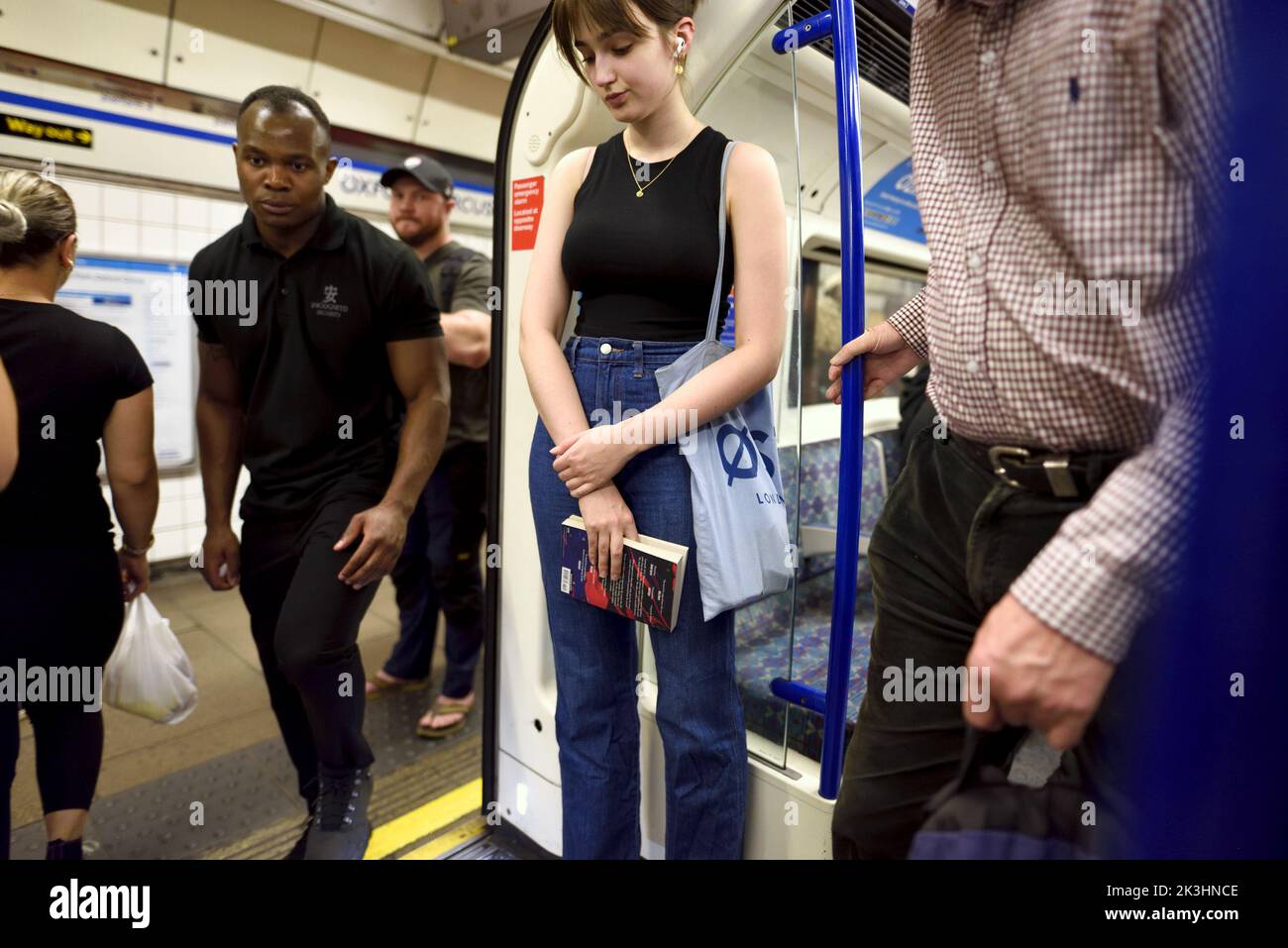 Londra, Inghilterra, Regno Unito. Giovane donna che tiene un libro su un treno della metropolitana Foto Stock