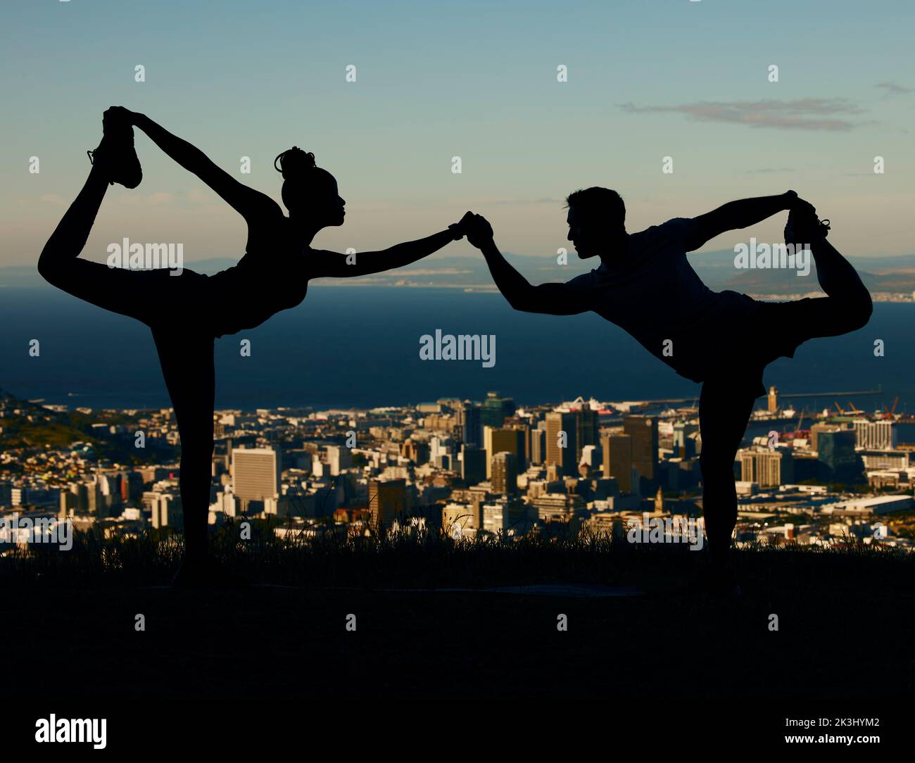 Silhouette di coppia che si allunga e fa yoga all'alba in città. Uomo e donna che si allenano, si allenano e si allenano insieme al tramonto. Persone Foto Stock
