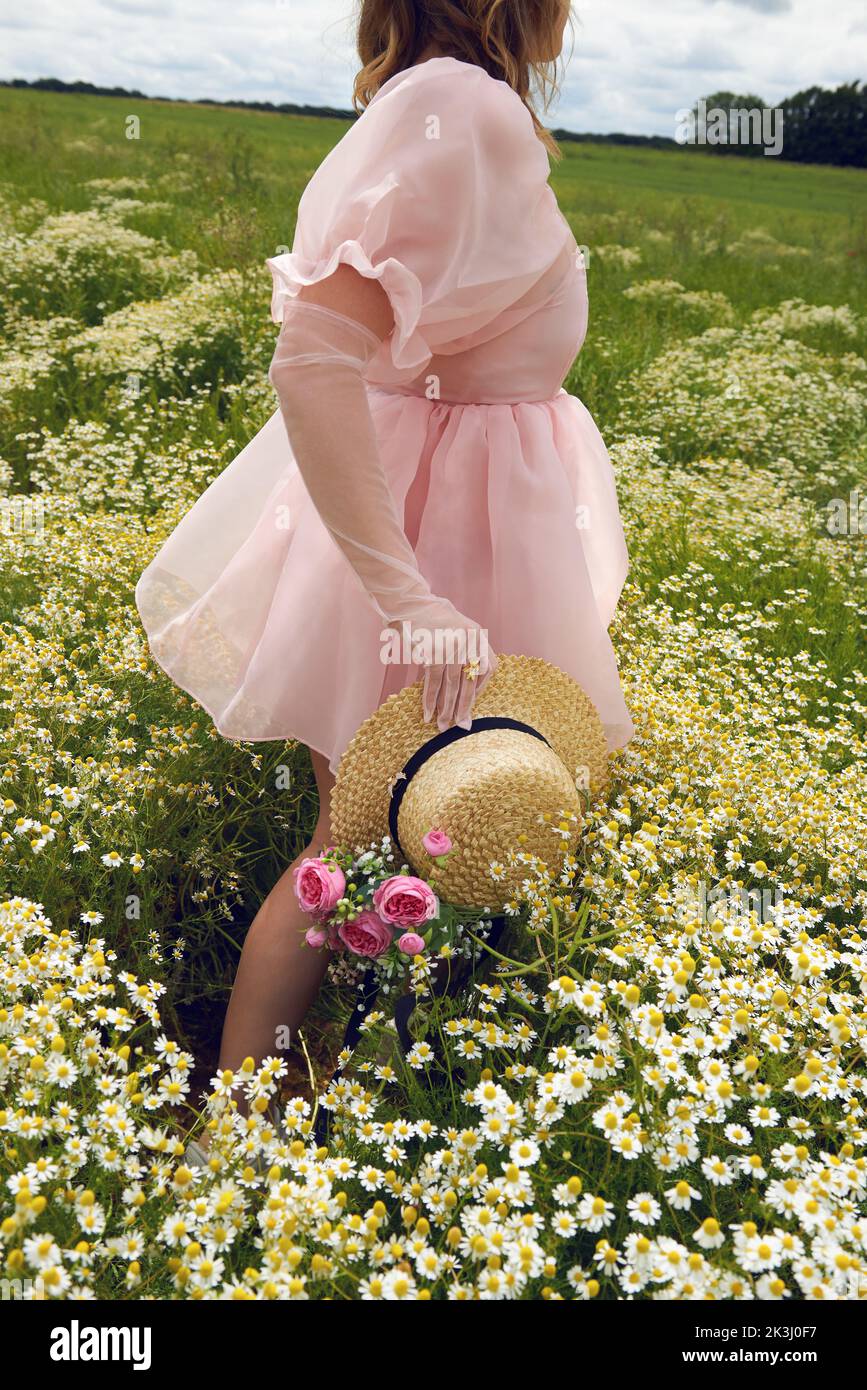 Giovane donna bionda che indossa un abito rosa puffy in un campo di fiori in estate Foto Stock
