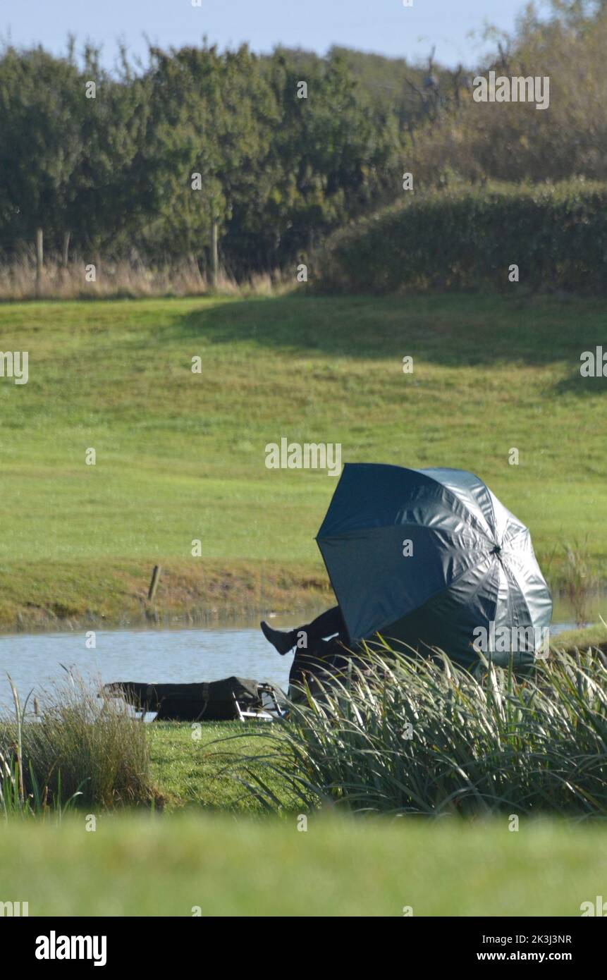 uomo solitario seduto sotto l'ombrello da pesca accanto al lago kent inghilterra Foto Stock