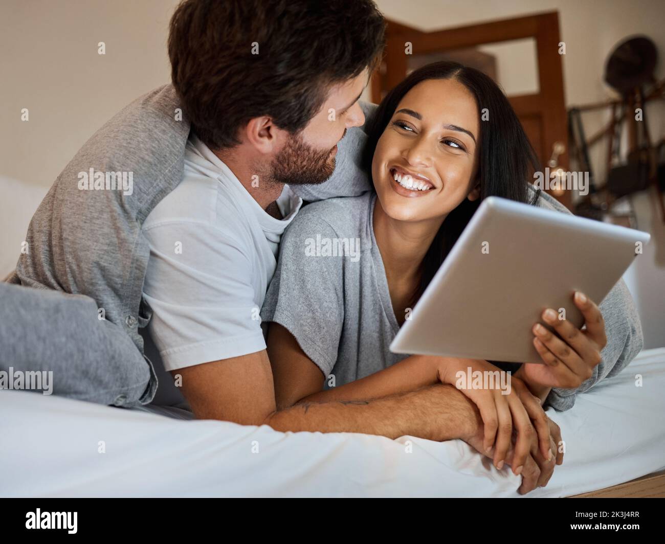 Coppia felice, sorriso e tablet in camera intrattenimento, amore e cura rilassarsi insieme a casa. Uomo e donna sorridenti per divertirsi a unire il tempo in streaming Foto Stock