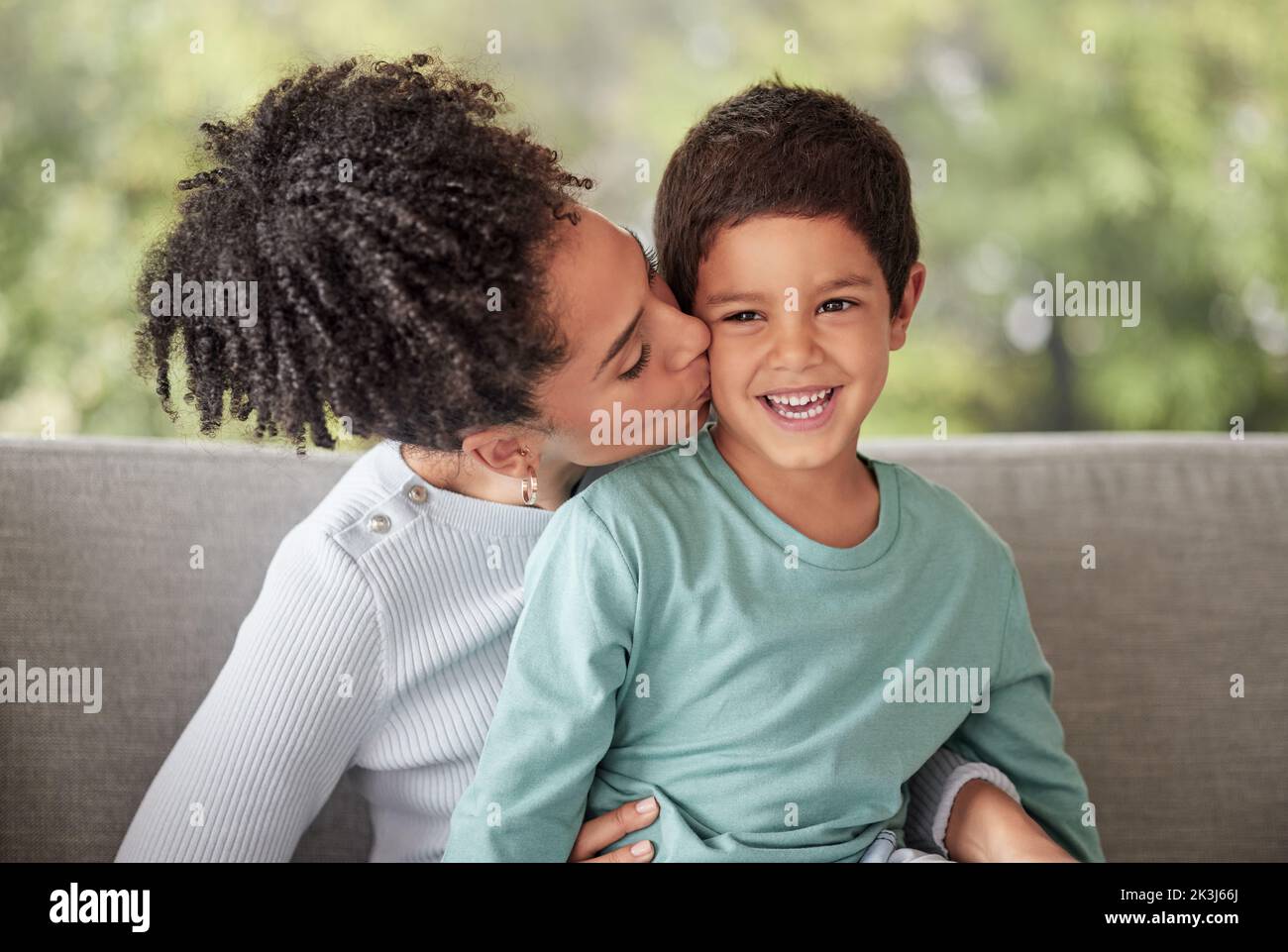 Famiglia felice, amore e madre bacia figlio su un divano, sorride e rilassarsi in un soggiorno insieme. Bambini, cura e genitore abbracciando il bambino, felice e. Foto Stock