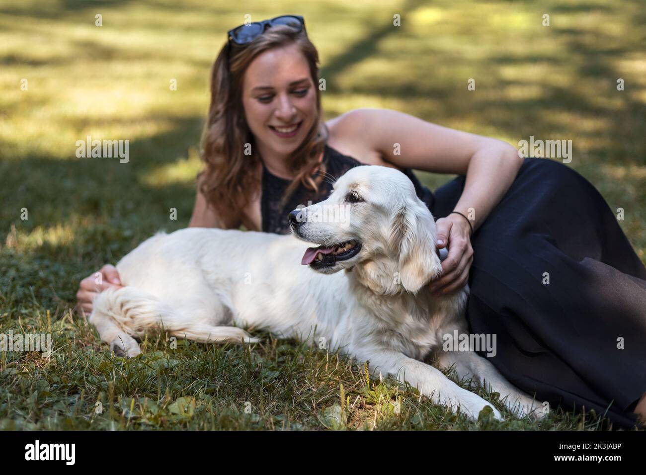 Giovane donna sdraiata in erba con un felice cane Golden Retriever Foto Stock