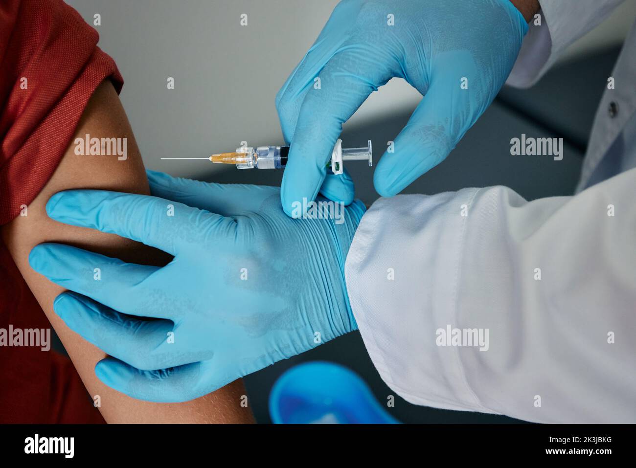 Mozzata di spalla del ragazzo durante l'iniezione del vaccino in una clinica medica. Vaccinazione dei bambini mentre pandemia globale Foto Stock