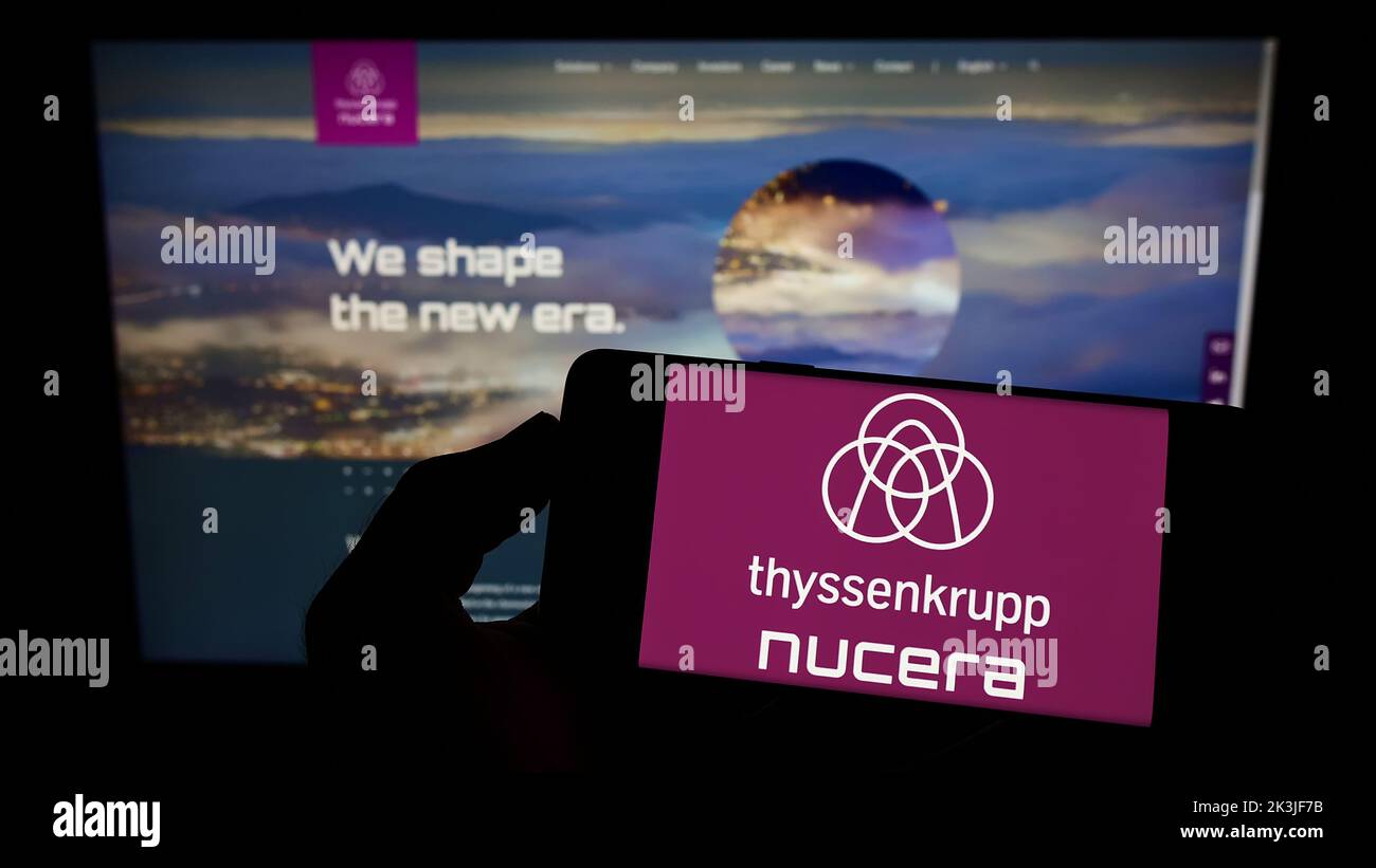 Persona che tiene il telefono cellulare con il logo della società thyssenkrupp nucera AG Co. KGaA sullo schermo di fronte alla pagina web aziendale. Messa a fuoco sul display del telefono. Foto Stock