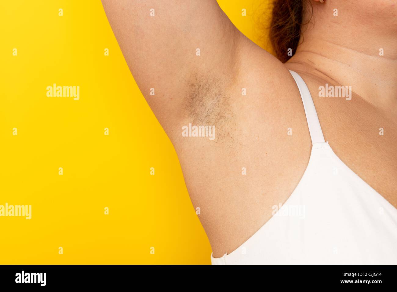 Donna toccare le ascelle pelose con la mano closeup, spazio copia libero, sfondo giallo. Braccio rialzato con capelli ascella. Tendenza bellezza femminile, libertà, femminismo Foto Stock