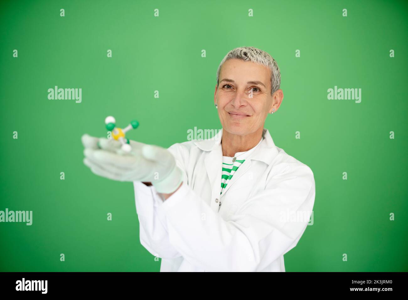 scienziato femminile con mantello bianco tiene in mano il modello di molecola e si trova di fronte allo sfondo verde Foto Stock