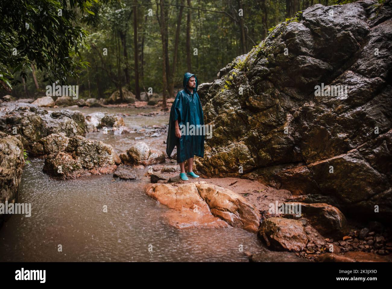 Uomo con impermeabile in piedi sotto la pioggia nel mezzo di una foresta tropicale Foto Stock