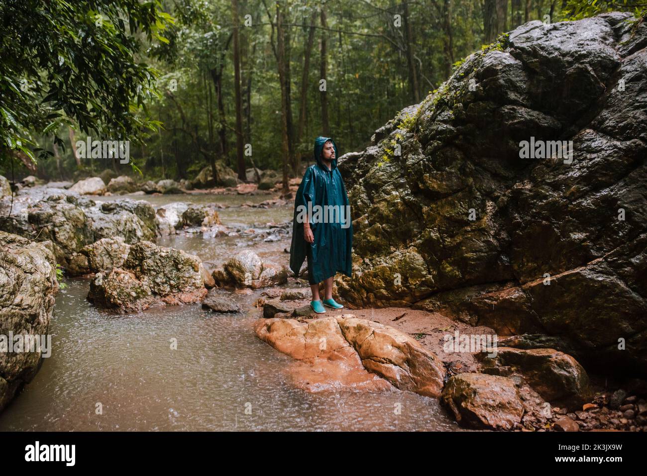 Uomo con impermeabile in piedi sotto la pioggia nel mezzo di una foresta tropicale Foto Stock