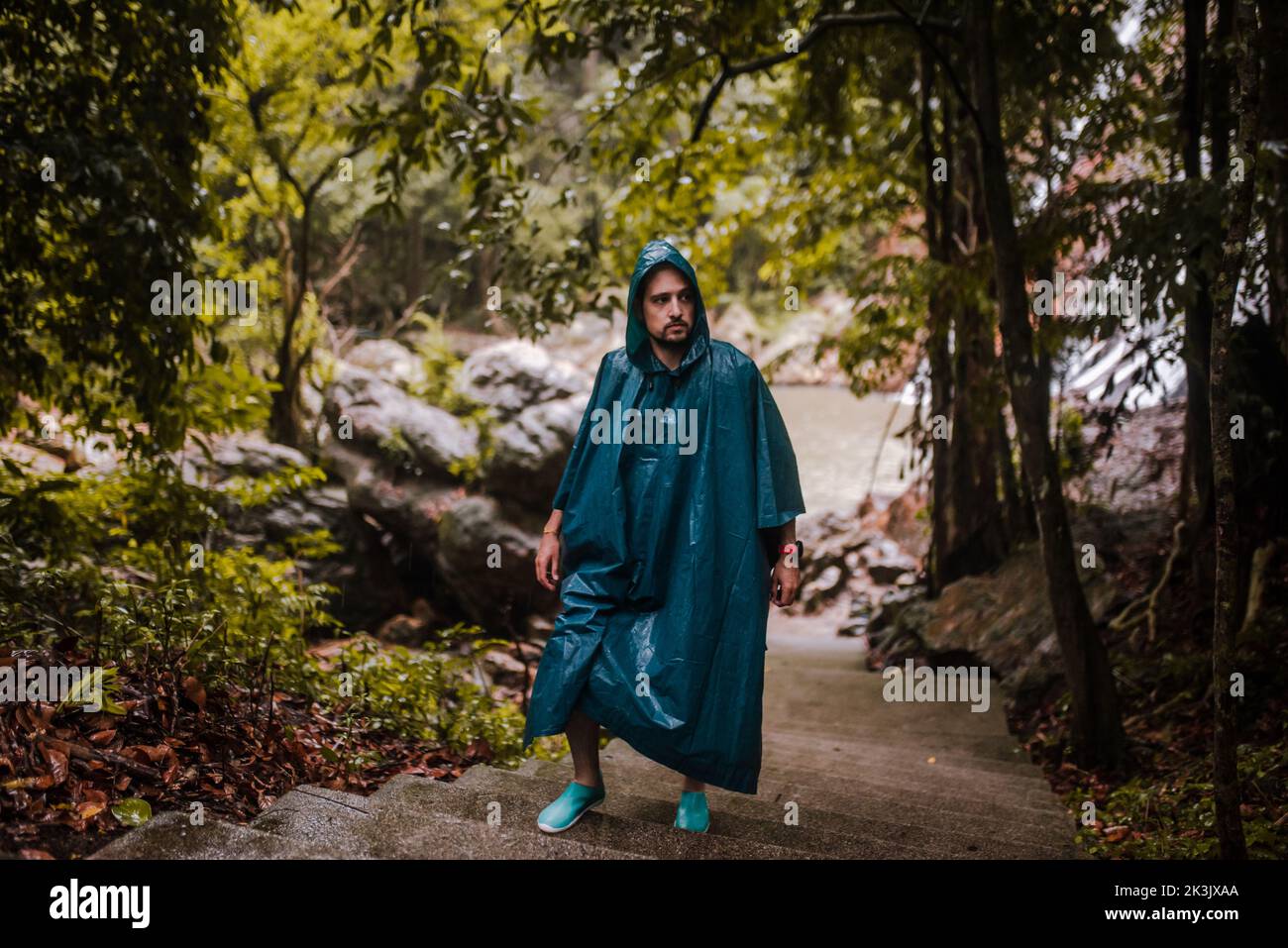 Uomo con un impermeabile che cammina attraverso una foresta Foto Stock