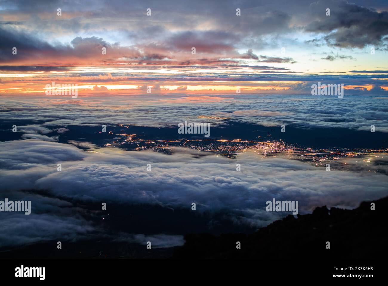 Guardando verso il basso sulle nuvole e le luci della città dalla cima del monte Fuji prima dell'alba Foto Stock