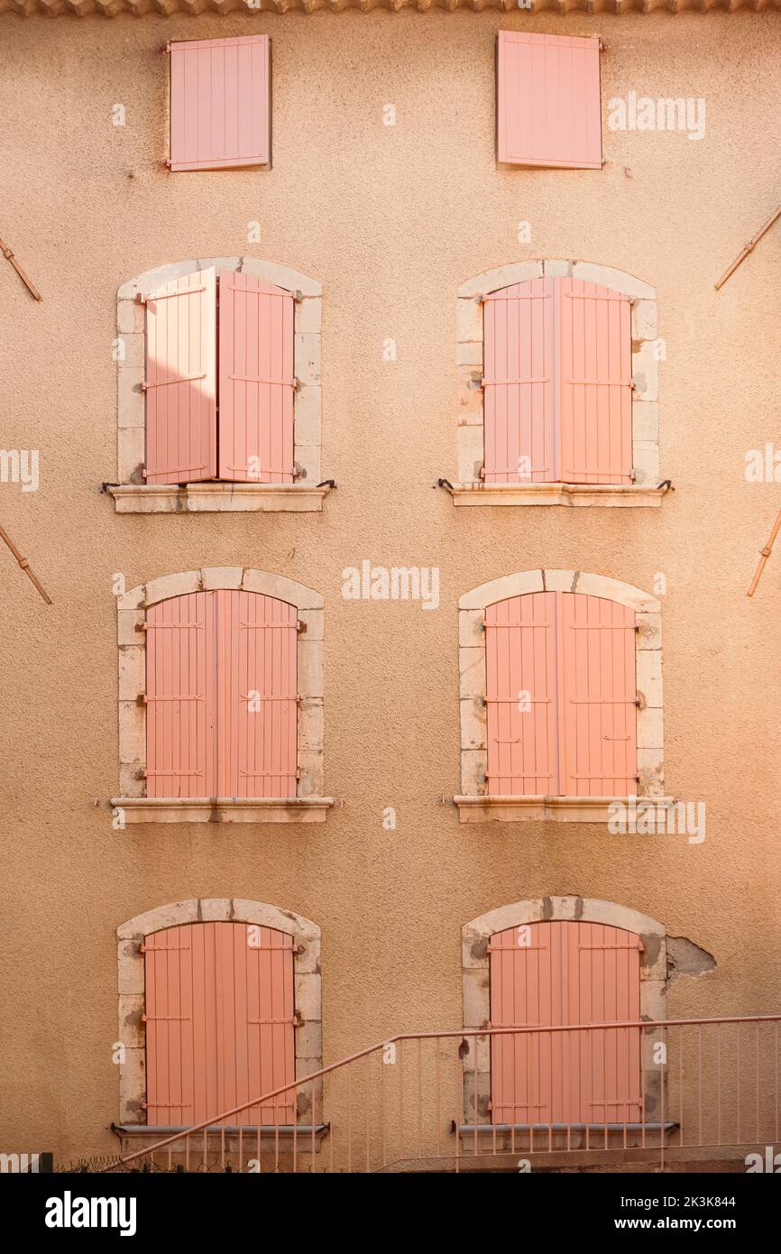 Molte persiane in legno rosa su pareti dipinte di color arancione pastello. Finestre chiuse di stile europeo con cornice ornamentale sulla facciata dell'edificio Foto Stock