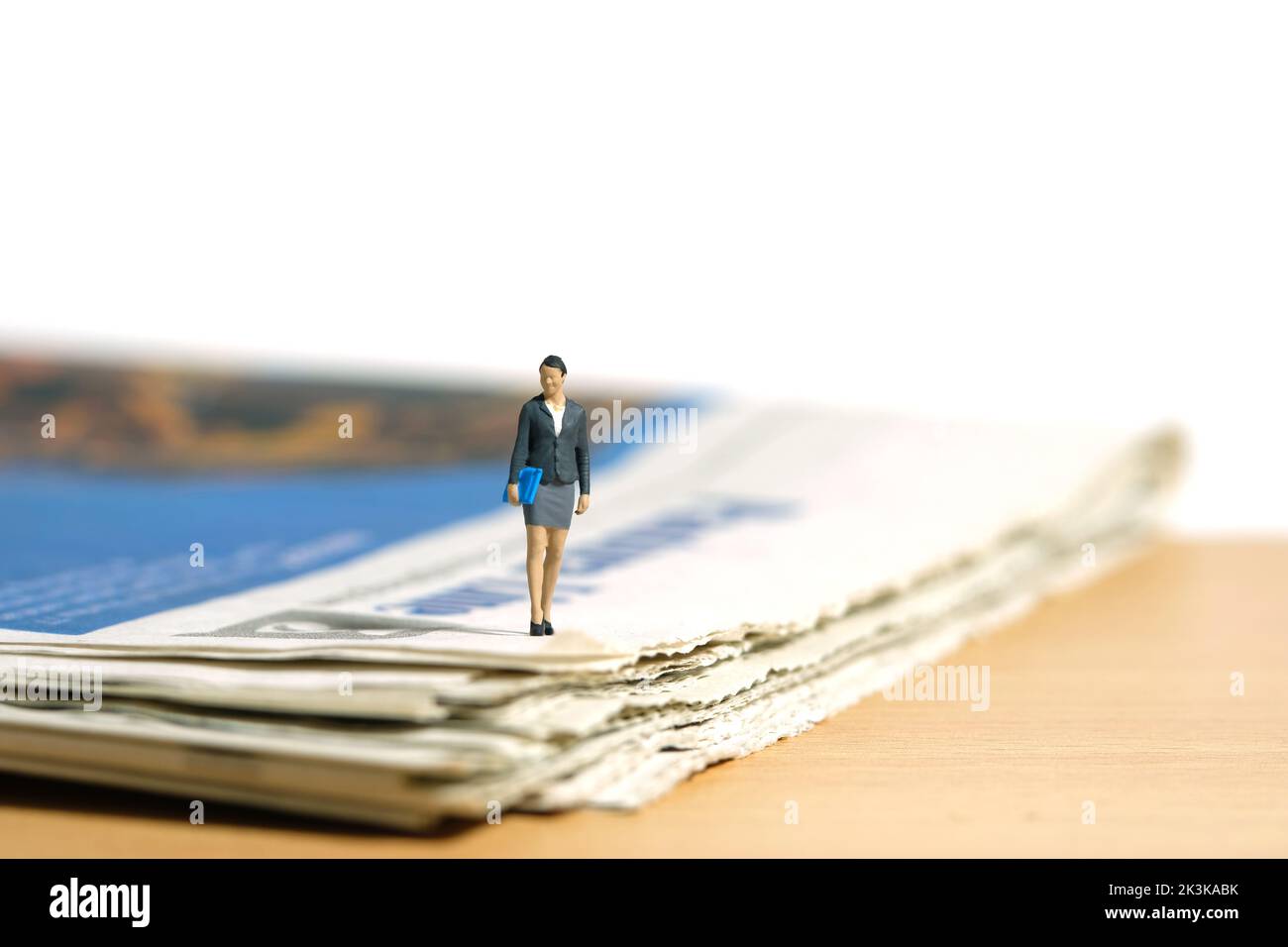 Fotografia di figura giocattolo delle persone in miniatura. Una donna d'affari che cammina con il giornale sulla scrivania. Isolato su sfondo bianco. Foto dell'immagine Foto Stock