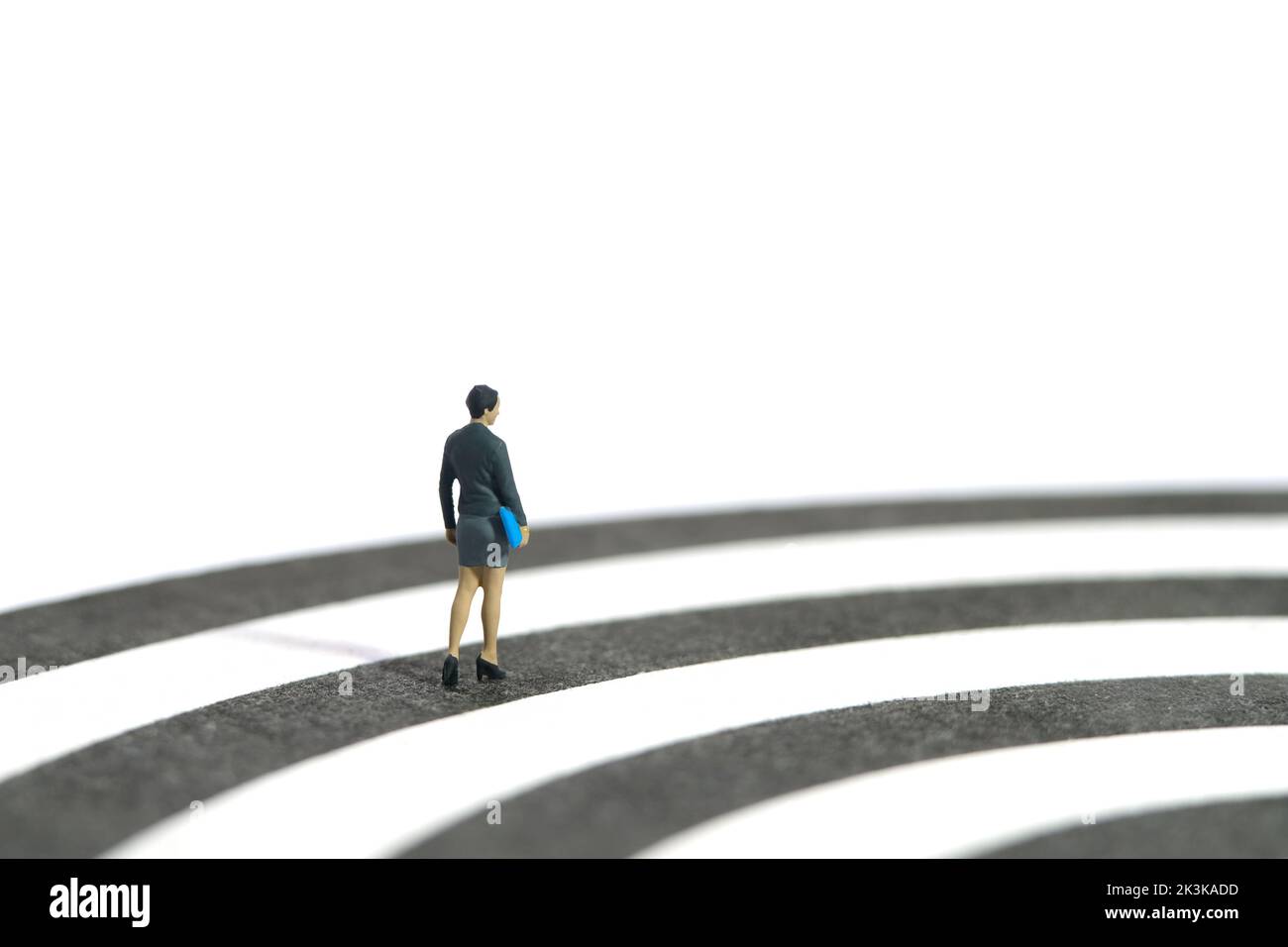 Fotografia di figura giocattolo delle persone in miniatura. Concetto di percorso professionale. Una donna d'affari che cammina sul dartboard. Isolato su sfondo bianco. Foto dell'immagine Foto Stock