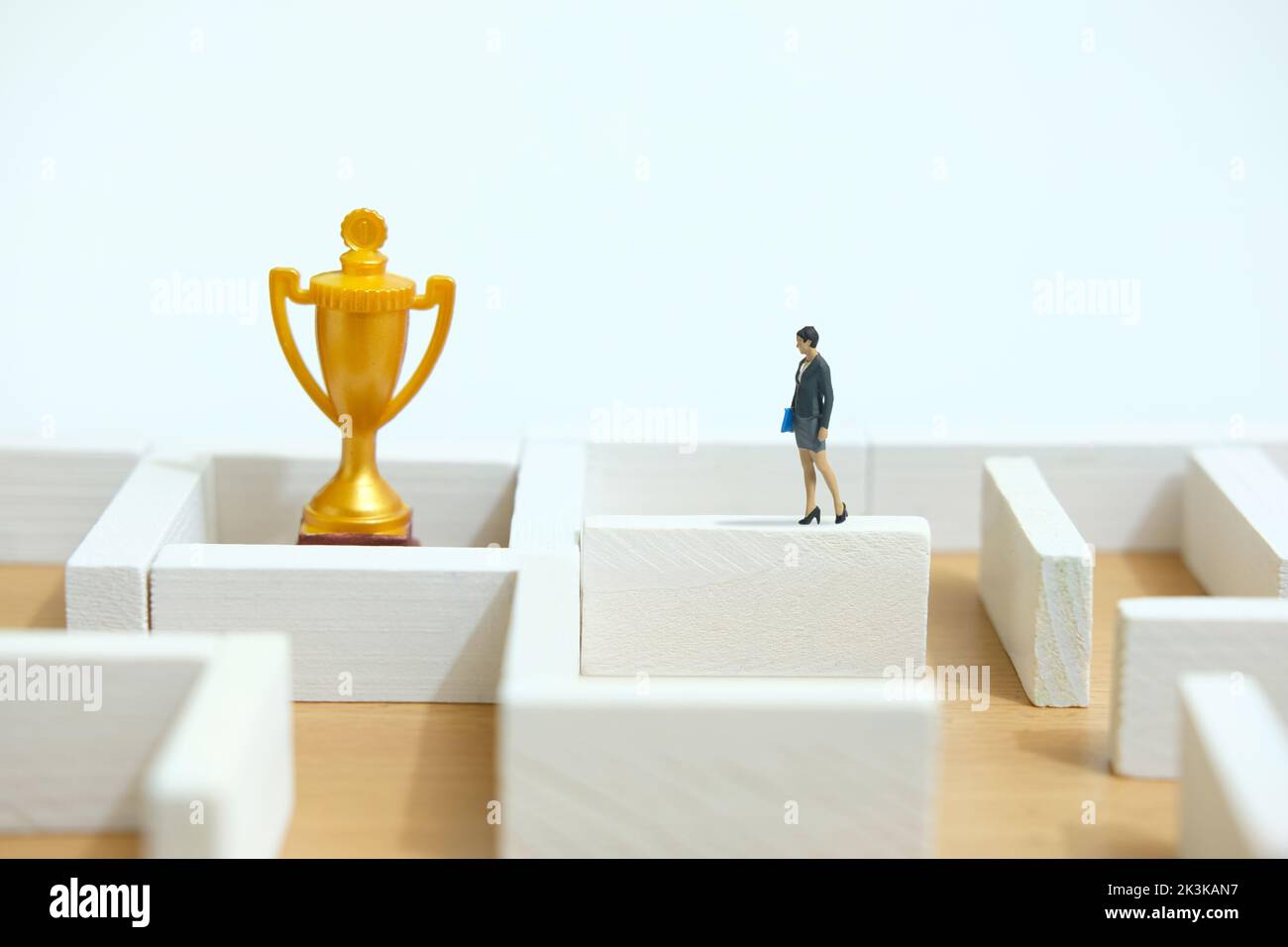 Fotografia di figura giocattolo delle persone in miniatura. Concetto di soluzione aziendale. Una donna d'affari che cammina sopra il labirinto labirinto muro alla ricerca di trofeo d'oro, solut Foto Stock