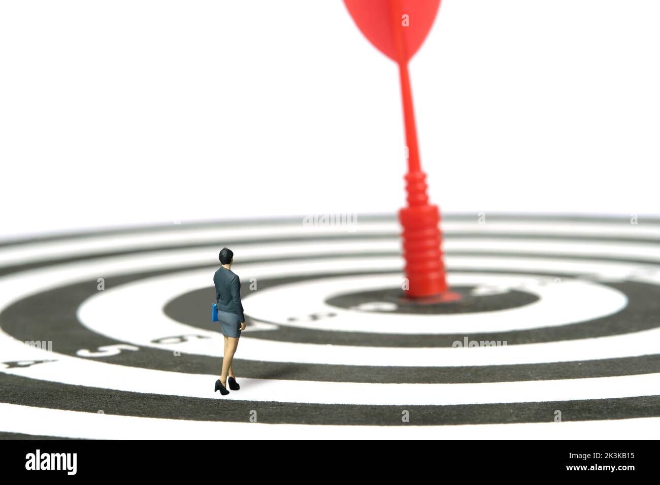 Fotografia di figura giocattolo delle persone in miniatura. Una donna d'affari in piedi sopra il dartboard camminando attraverso una freccia rossa nel centro. Isolato su sfondo bianco Foto Stock