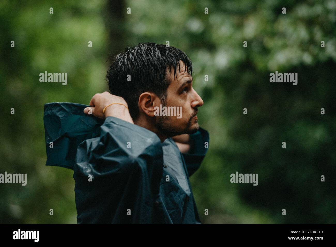 Uomo che indossa un impermeabile che gli indossa il cappuccio nel mezzo di una foresta Foto Stock