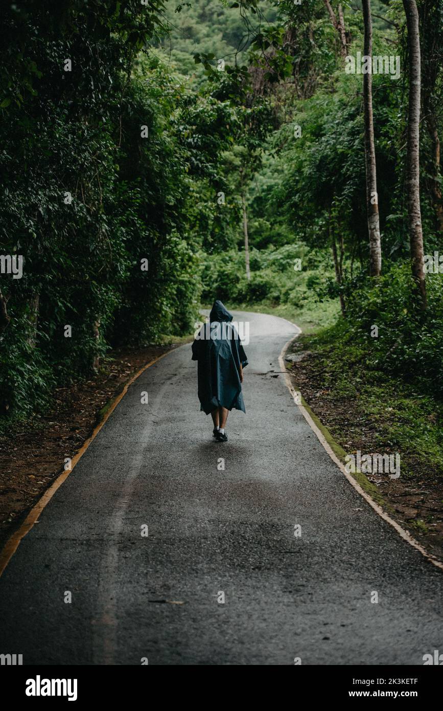 Uomo che indossa un impermeabile che cammina nel mezzo di una strada Foto Stock