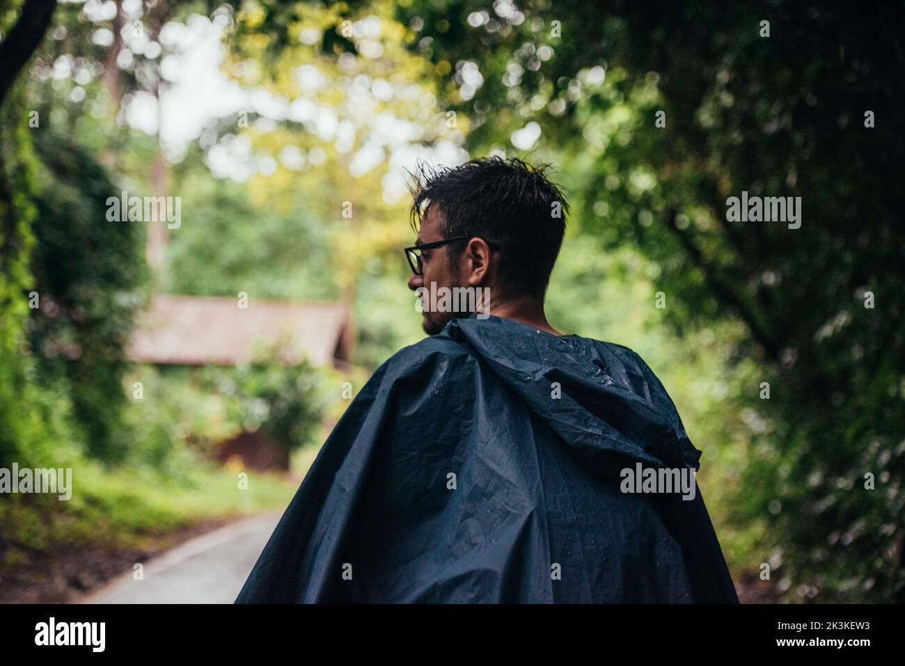 Uomo che indossa un impermeabile che cammina nel mezzo di una strada vicino alla foresta Foto Stock