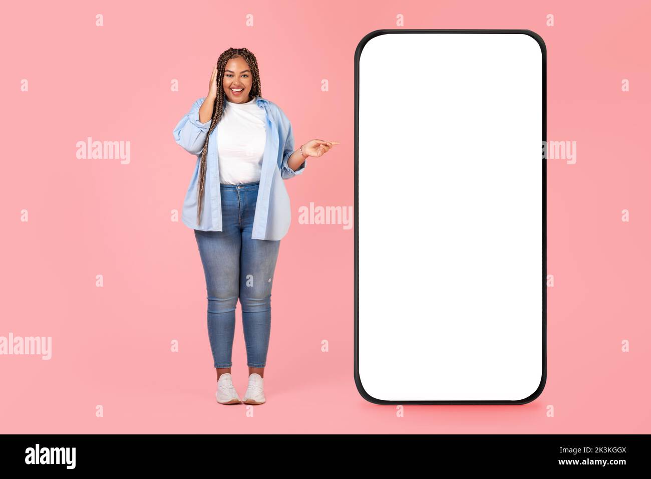 Donna nera felice che indica lo schermo del telefono grande, sfondo rosa Foto Stock