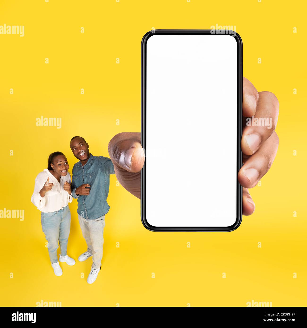 Allegra coppia nera che mostra l'enorme schermo del telefono su sfondo giallo Foto Stock