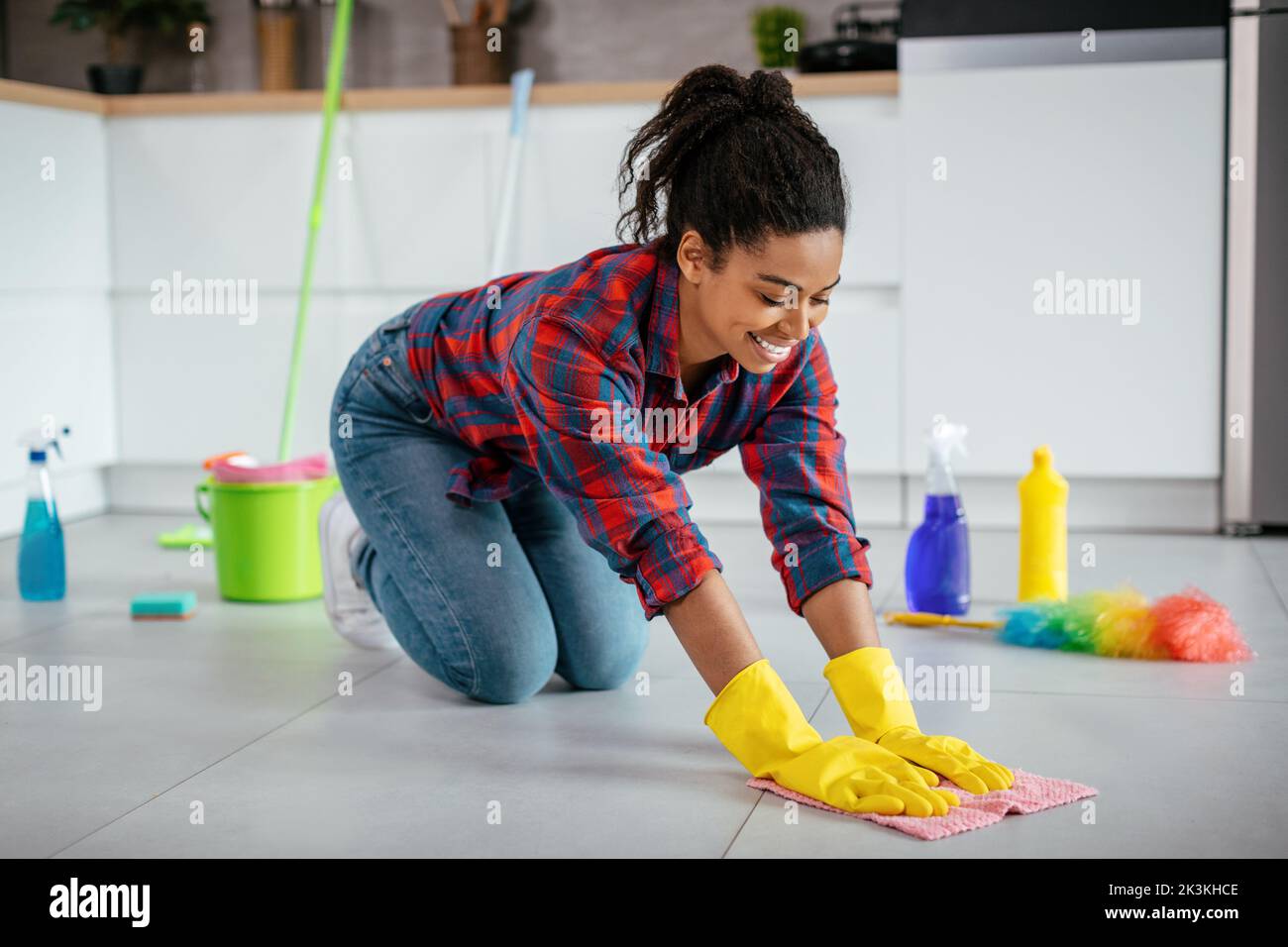 Felice giovane casalinga nero pavimento di pulizia con i rifornimenti di pulizia, godere di pulizia in cucina interna Foto Stock