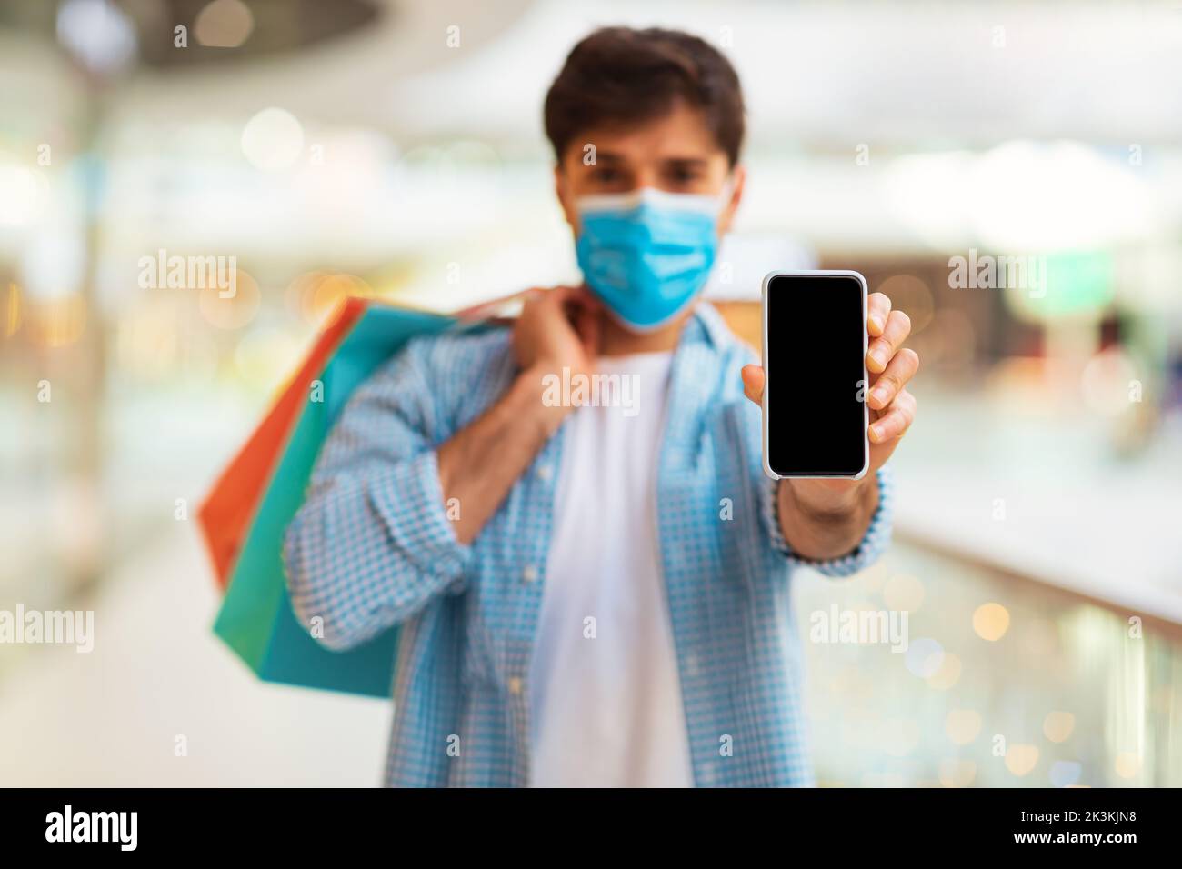 Uomo che mostra lo schermo del telefono che indossa la maschera facciale Shopping nel centro commerciale Foto Stock
