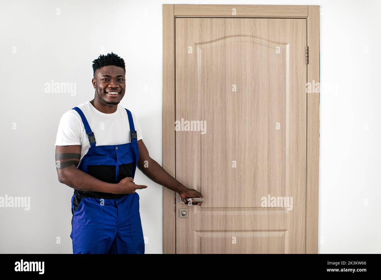 Lavoratore maschio nero che punta alla nuova porta dopo l'installazione in ambienti interni Foto Stock