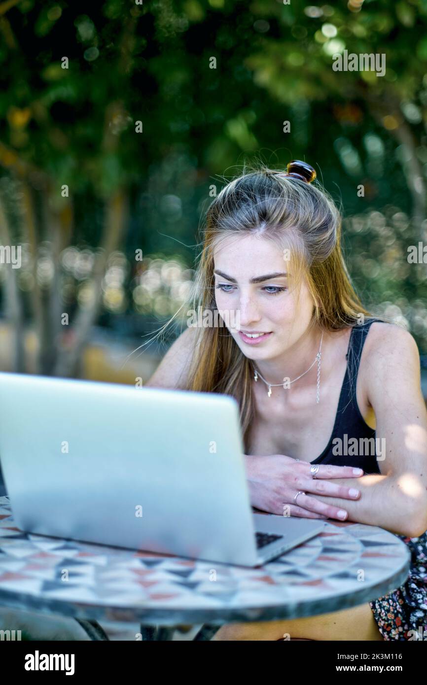 Ritratto di una giovane donna caucasica in posa all'aperto in un giardino con un computer portatile in cerca di informazioni in internet. Concetto di stile di vita. Foto Stock