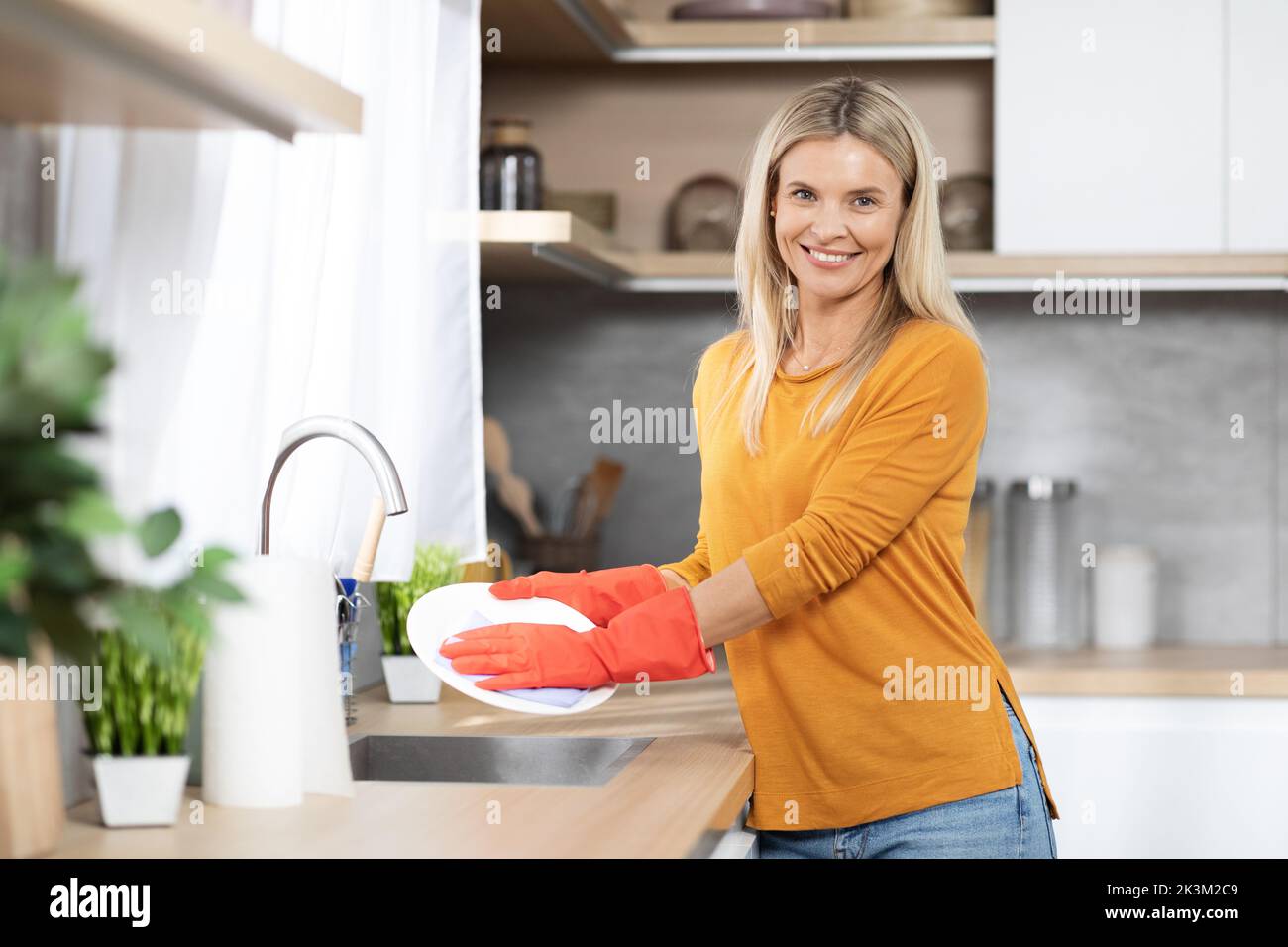 Allegro bella donna bionda lavare piatti a casa Foto Stock