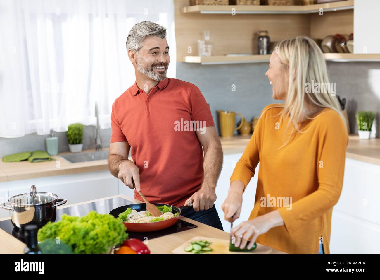 Allegri sposi di mezza età che cucinano e conversano Foto Stock