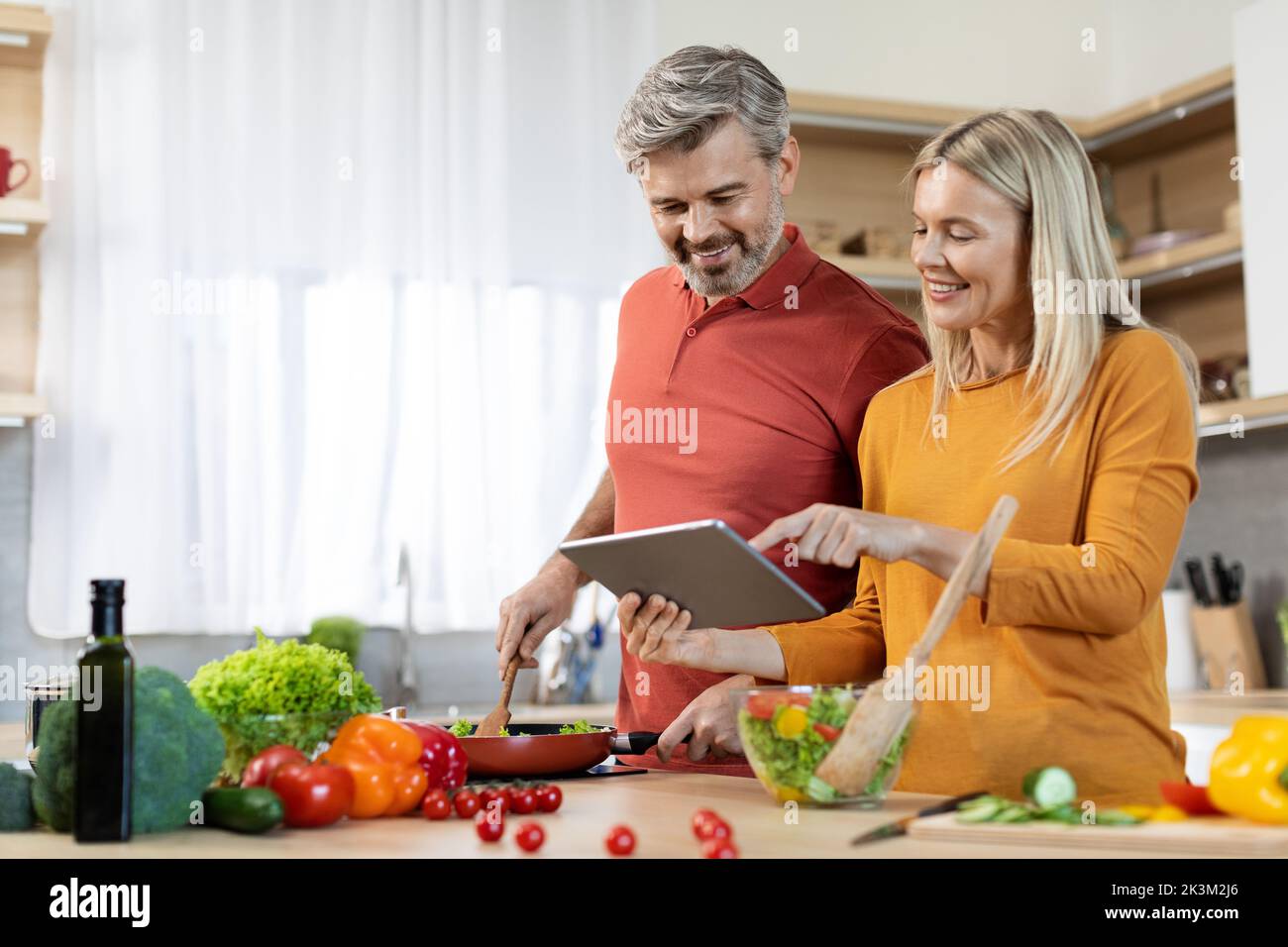 Felice coppia di mezza età cucina sana cena, controllando le ricette on-line Foto Stock