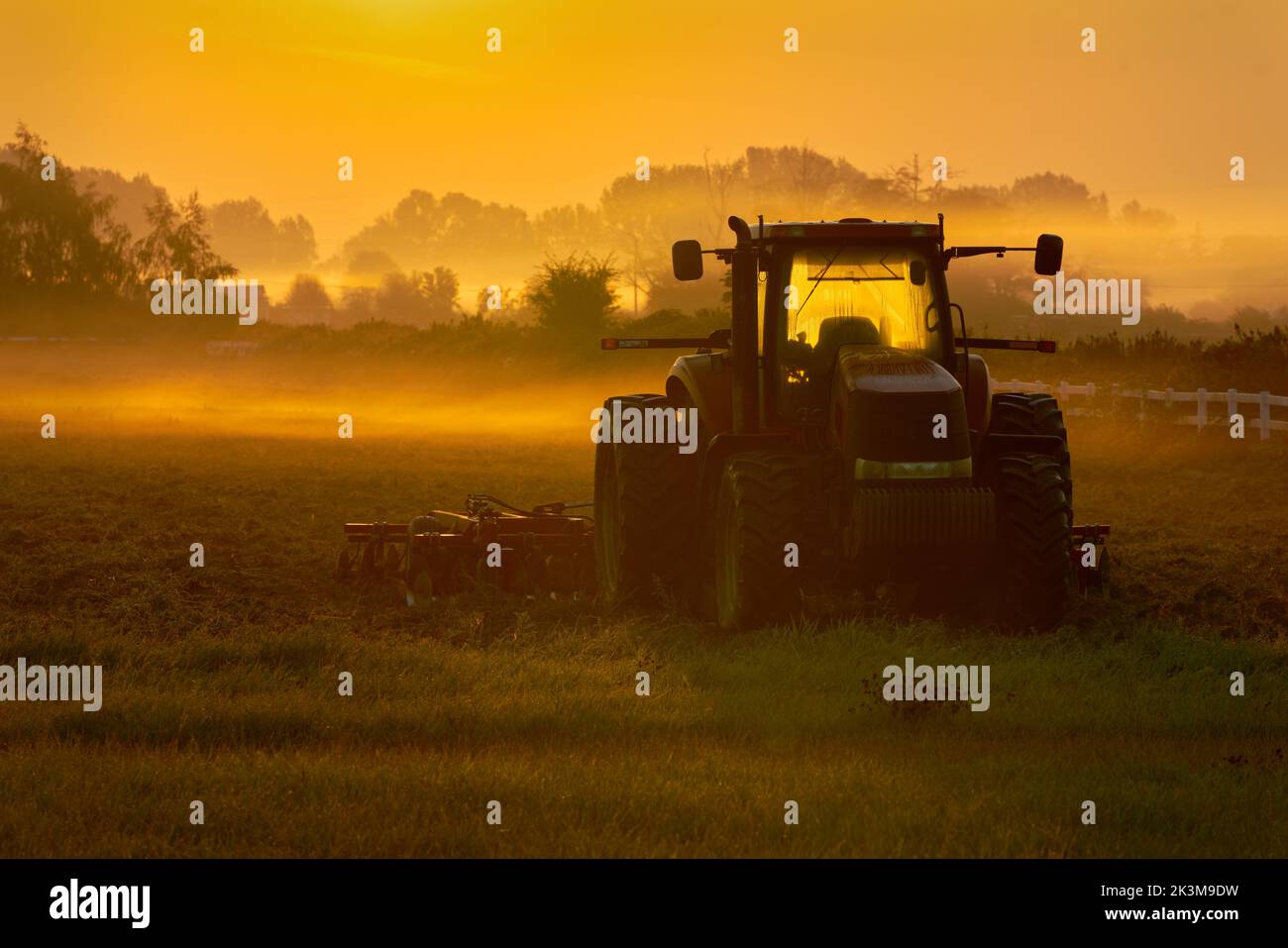 Foggy mattina Farm Field Alba. Colori dell'alba su un campo e trattore di fattoria misty. Foto Stock