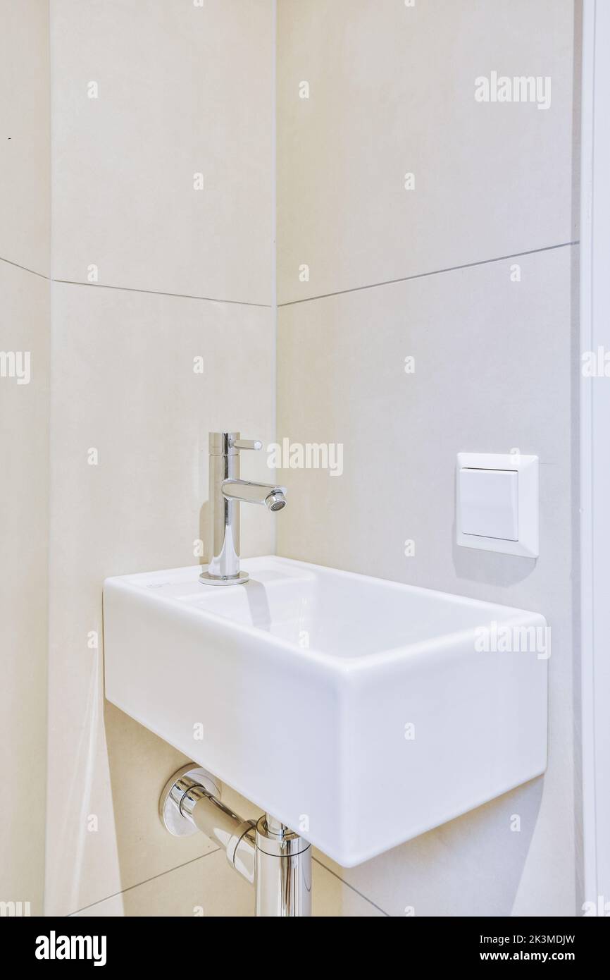 Lavello in ceramica bianca con rubinetto cromato lucido installato su parete beige in bagno Foto Stock