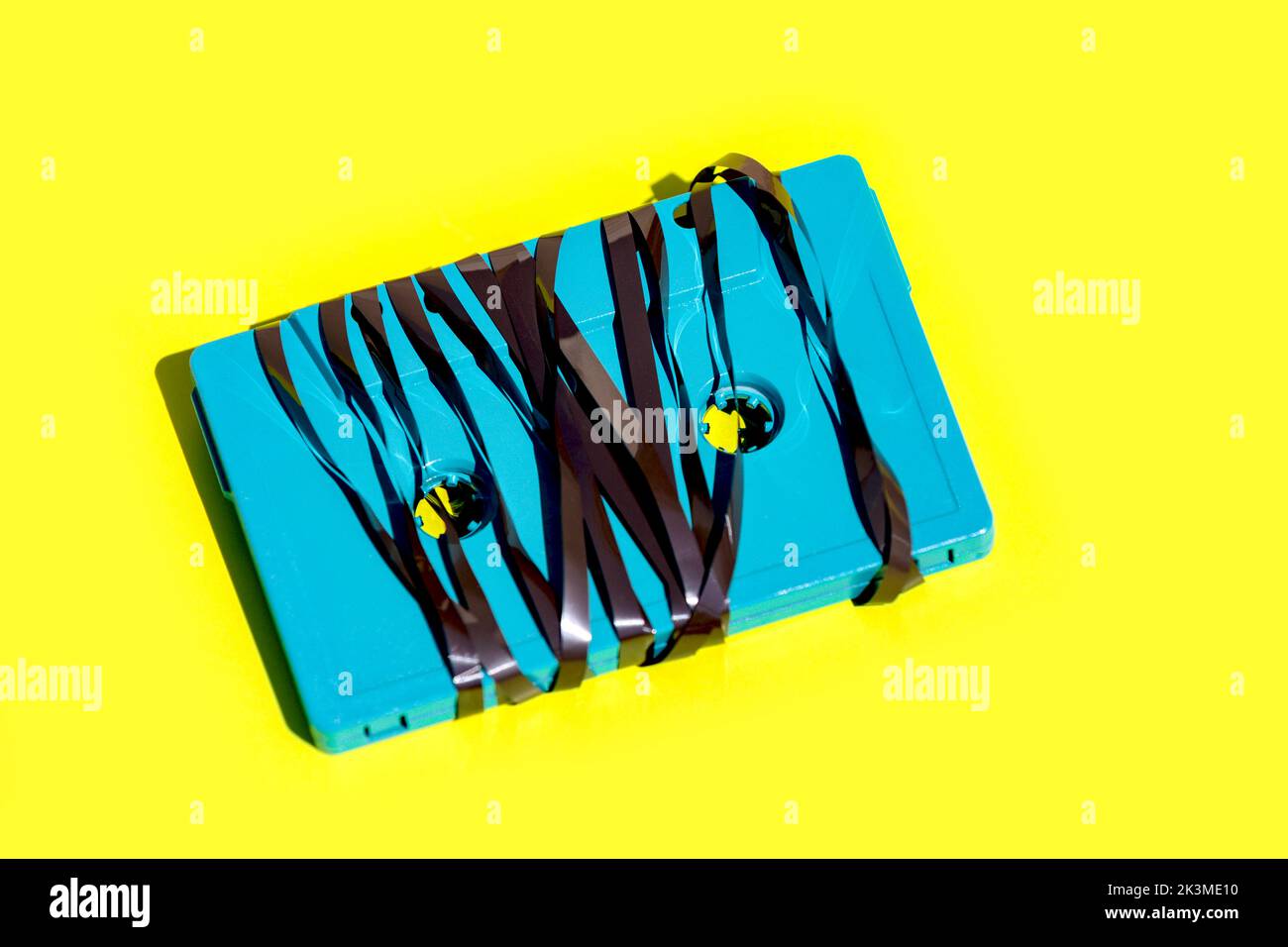 Dall'alto della vecchia cassetta audio blu con nastro magnetico aggrovigliato collocato su sfondo giallo vibrante in studio Foto Stock